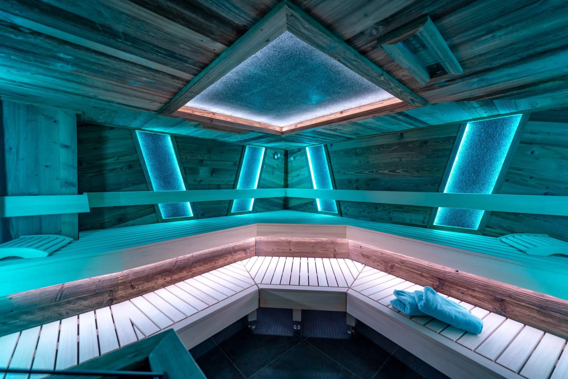 Eventsauna mit türkis beleuchteter Holzverkleidung und mehrstufigen Bänken