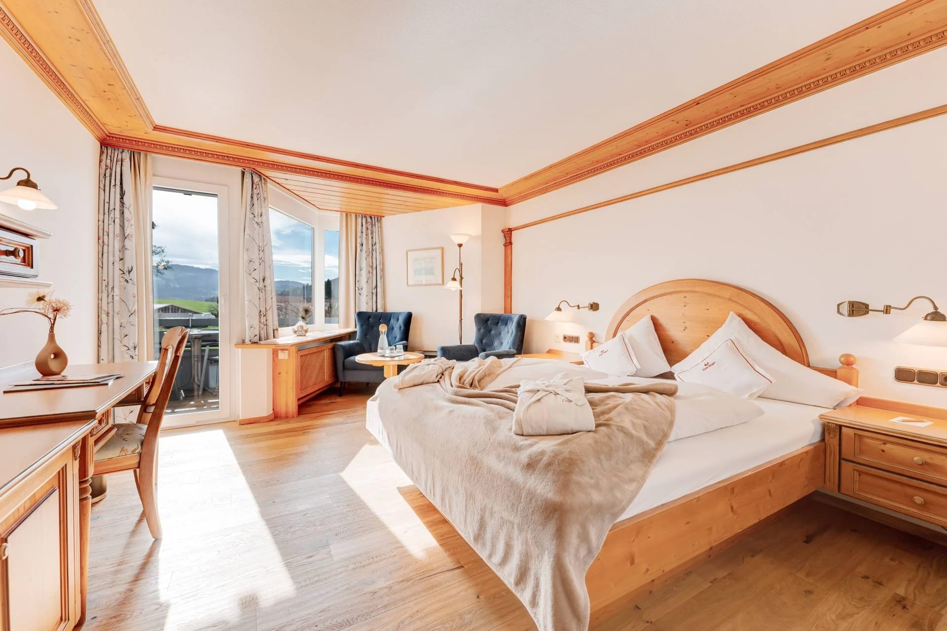 Doppelzimmer mit Holzdecke, hellem Bettbereich und Balkontür mit Bergblick