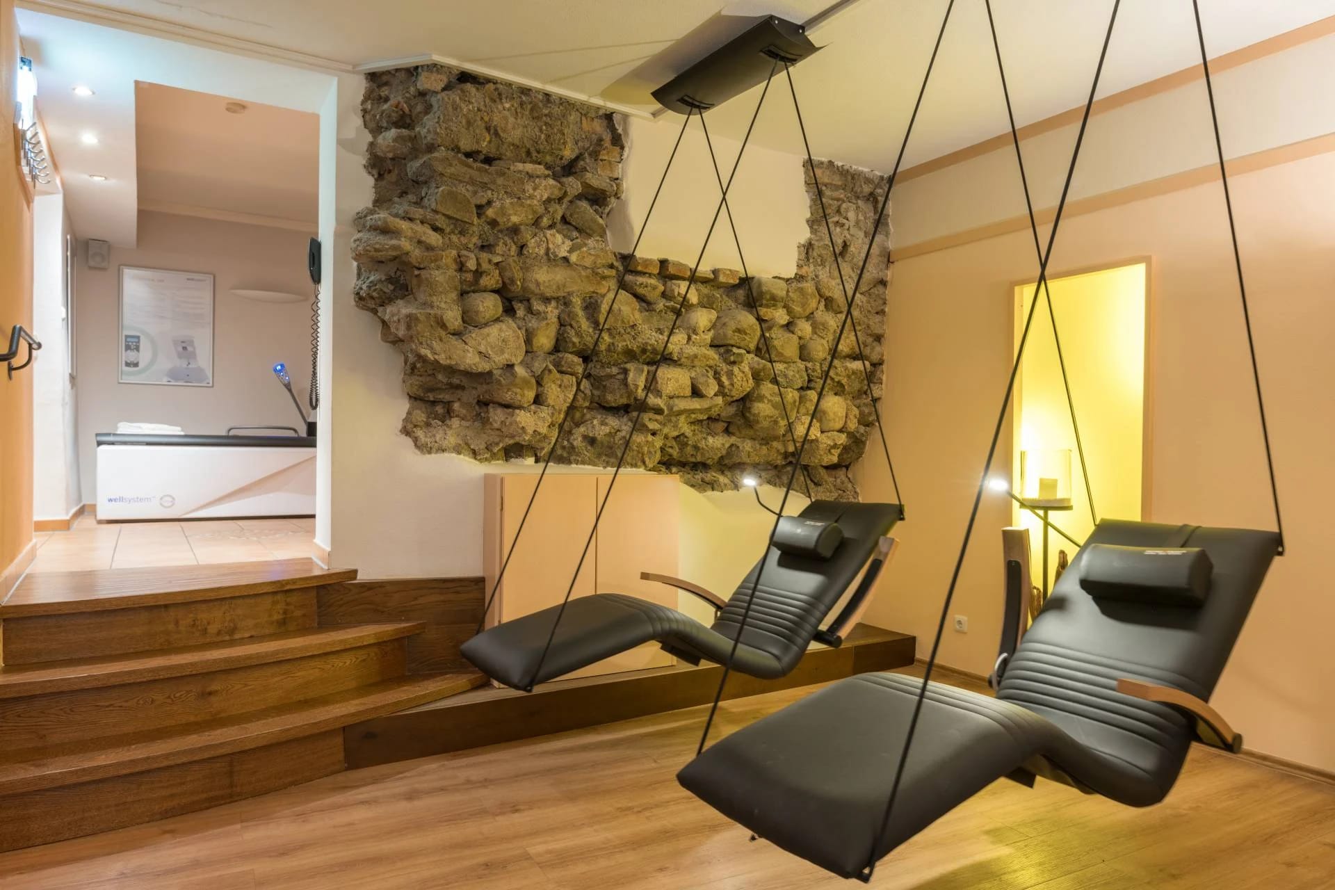 Zwei schwebende Liegen aus schwarzem Leder vor einer Natursteinwand im Wellnessbereich