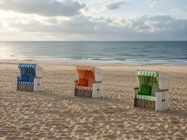 Drei bunte Strandkörbe am breiten Sandstrand mit Blick auf die Nordsee
