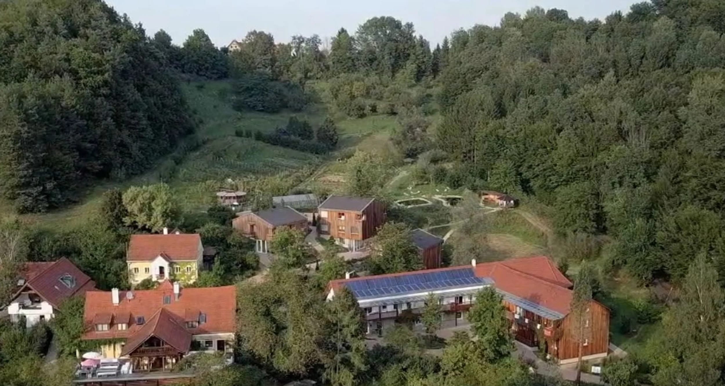 Luftaufnahme des Resorts mit Holzhäusern und Gärten in der Hügellandschaft