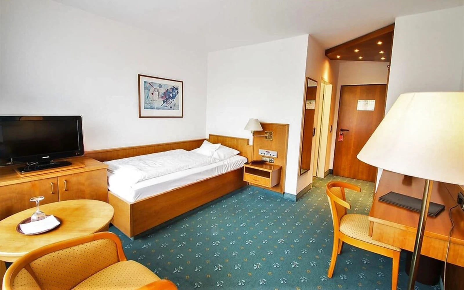 Einzelzimmer mit Bett, Schreibtisch, Sesseln und Fernseher
