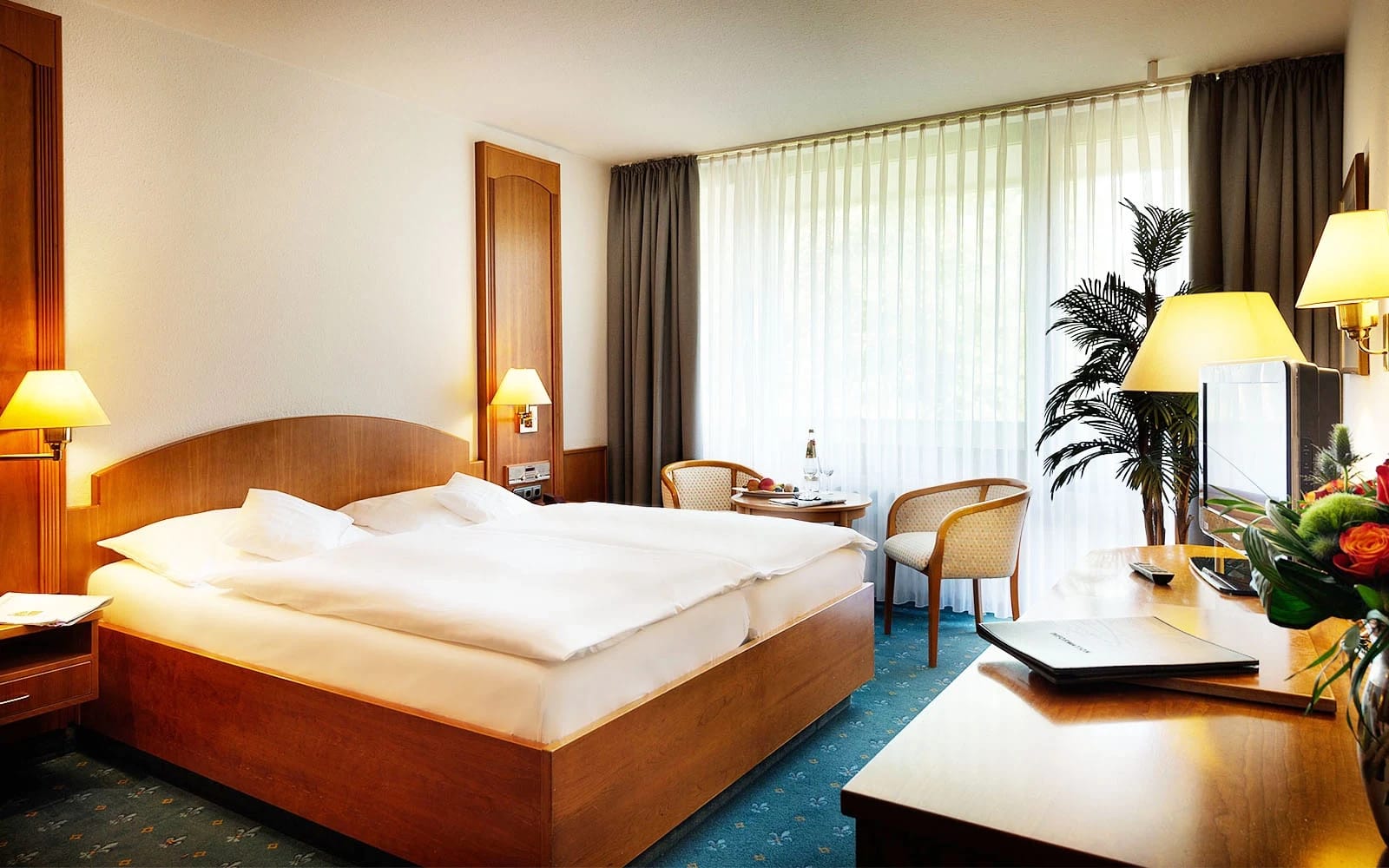 Doppelzimmer mit Holzbett, Sitzecke am bodentiefen Fenster und dunklen Vorhängen