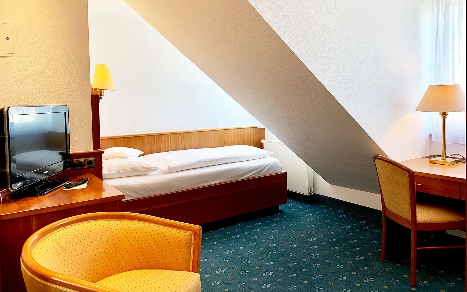 Einzelzimmer unter der Dachschräge mit Bett, Schreibtisch und Sessel