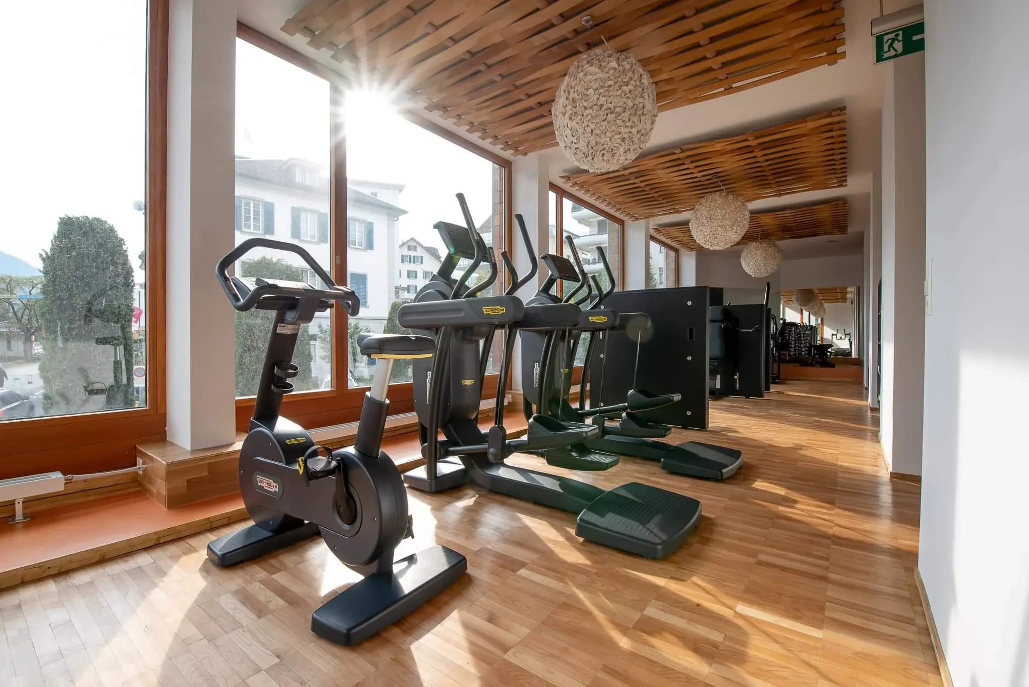 Fitnessraum mit Ergometer, Crosstrainern und Steppern vor großen Fenstern