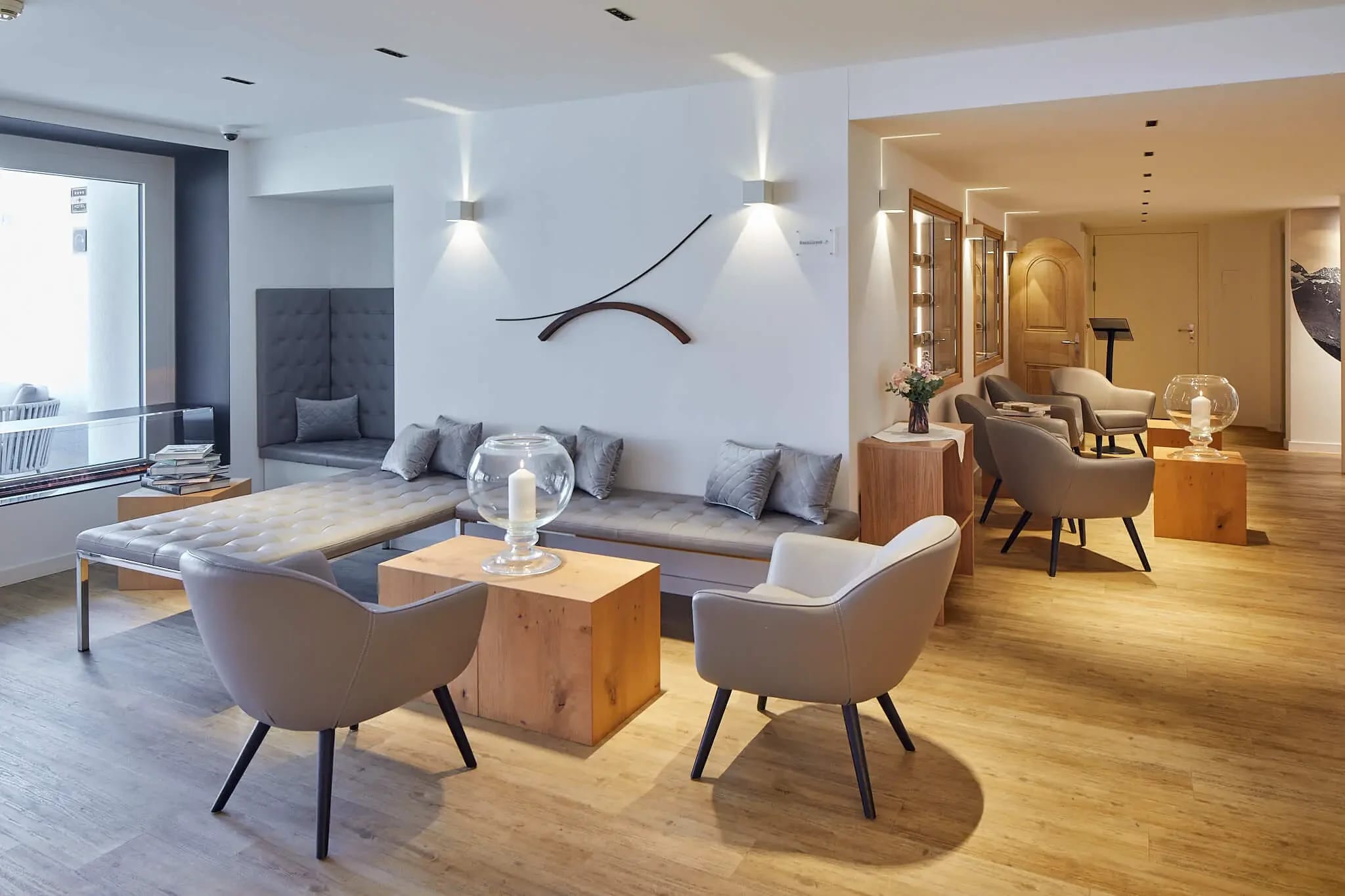 Lounge mit langer gepolsterter Sitzbank, Sesseln, Holzwürfeln als Tischen und hellem Holzboden