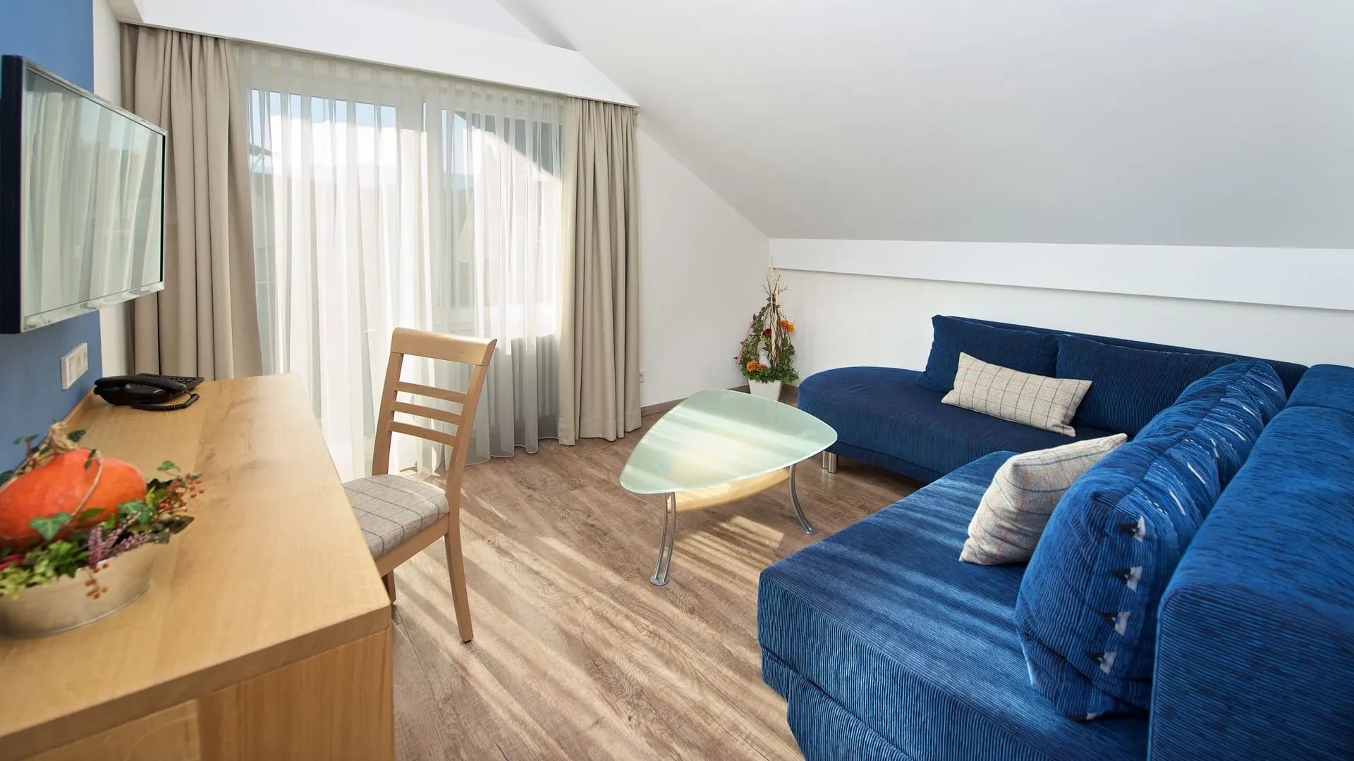 Wohnbereich mit blauer Eckcouch, Glastisch, Stuhl und Balkontür