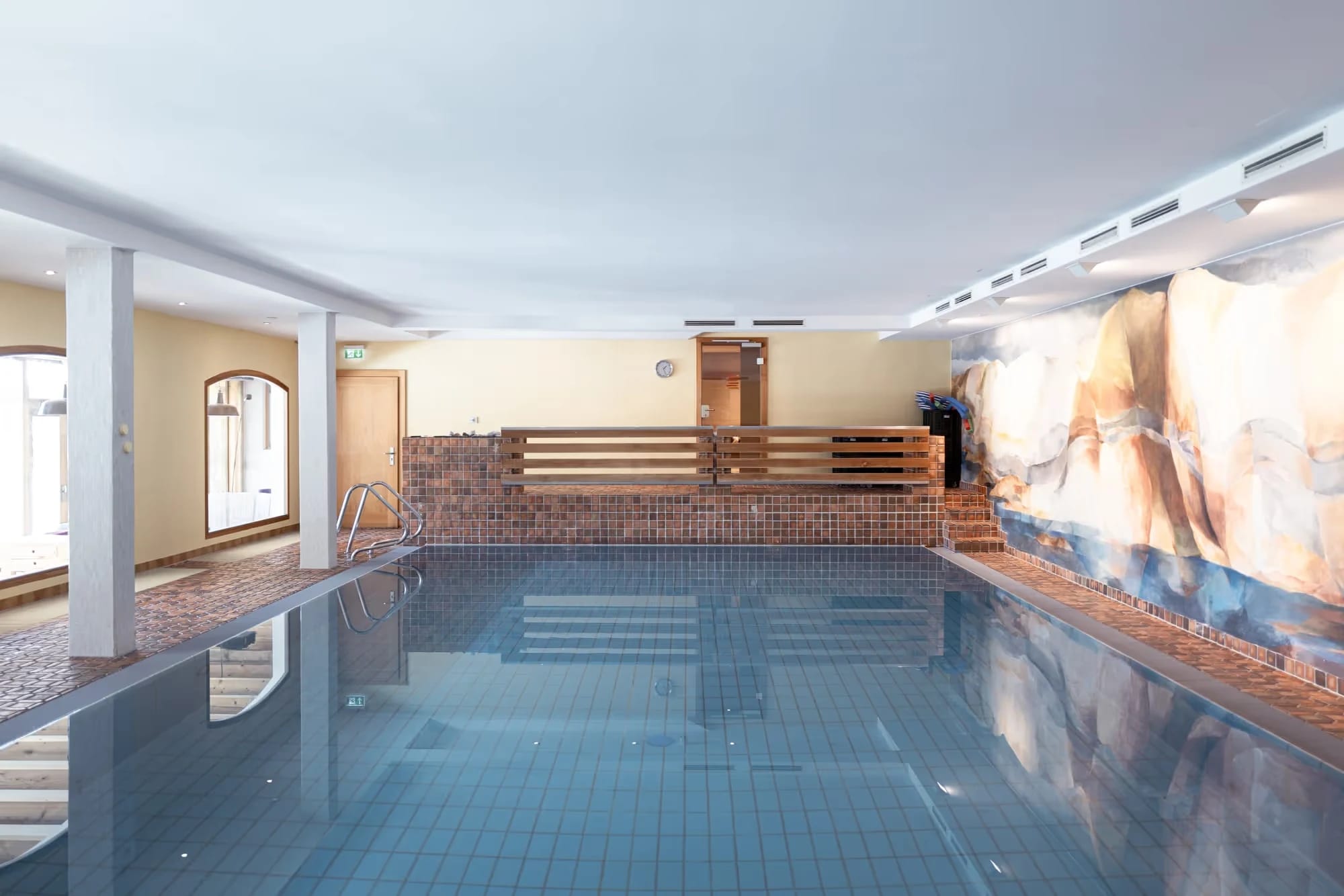 Hallenbad im Tannerhof mit Mosaikfliesen, Holzgeländer und Bergmotiv an der Wand