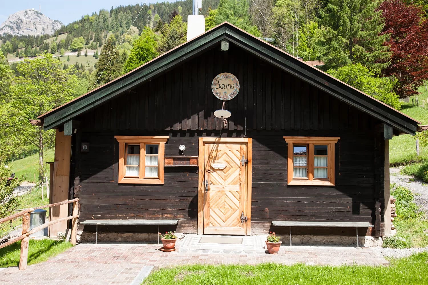 Traditionelles dunkles Saunahäuschen mit Holztür und Fenstern in grüner Berglandschaft