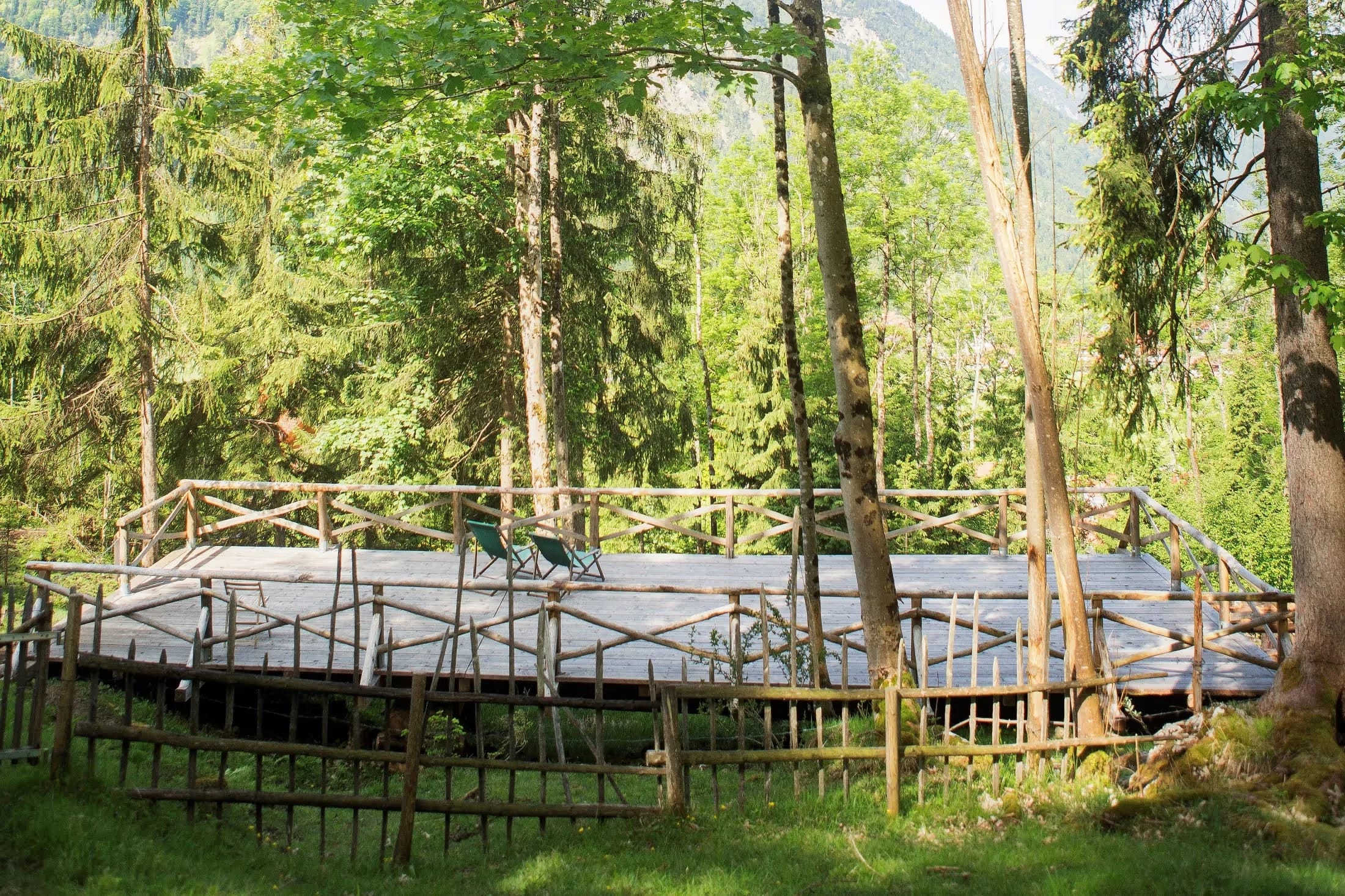 Hölzernes Sonnendeck im Wald mit Liegestühlen, umgeben von hohen Bäumen und Bergen