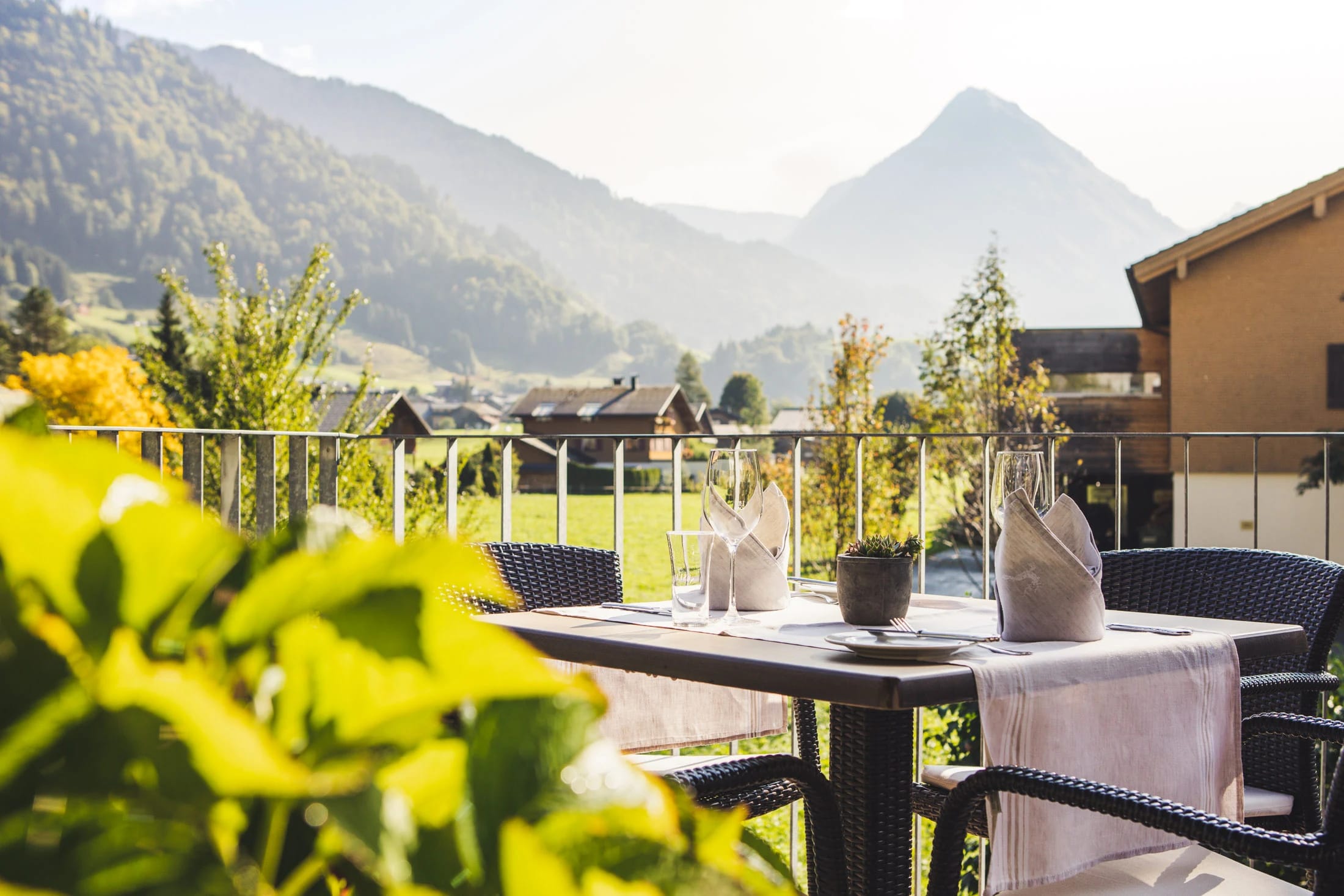 Gedeckter Tisch auf der Terrasse mit Blick über Wiesen auf die Berge