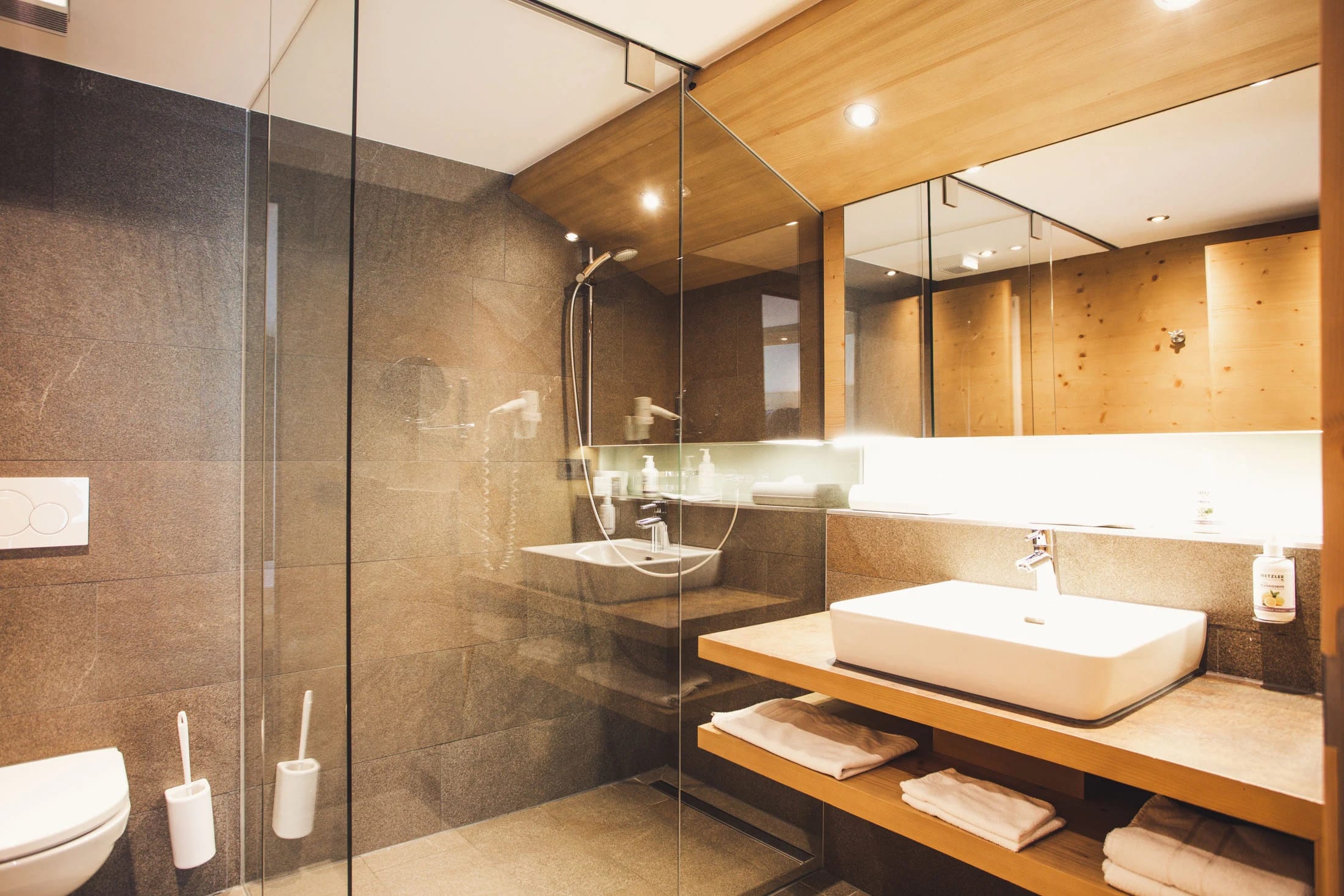 Badezimmer mit gläserner Dusche, Waschtisch aus Holz und Steinfliesen