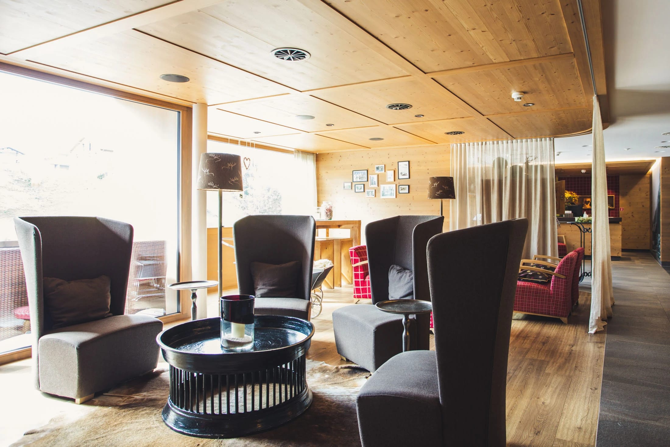 Lounge mit hohen Polstersesseln um einen runden Tisch, Holzdecke und großem Fenster