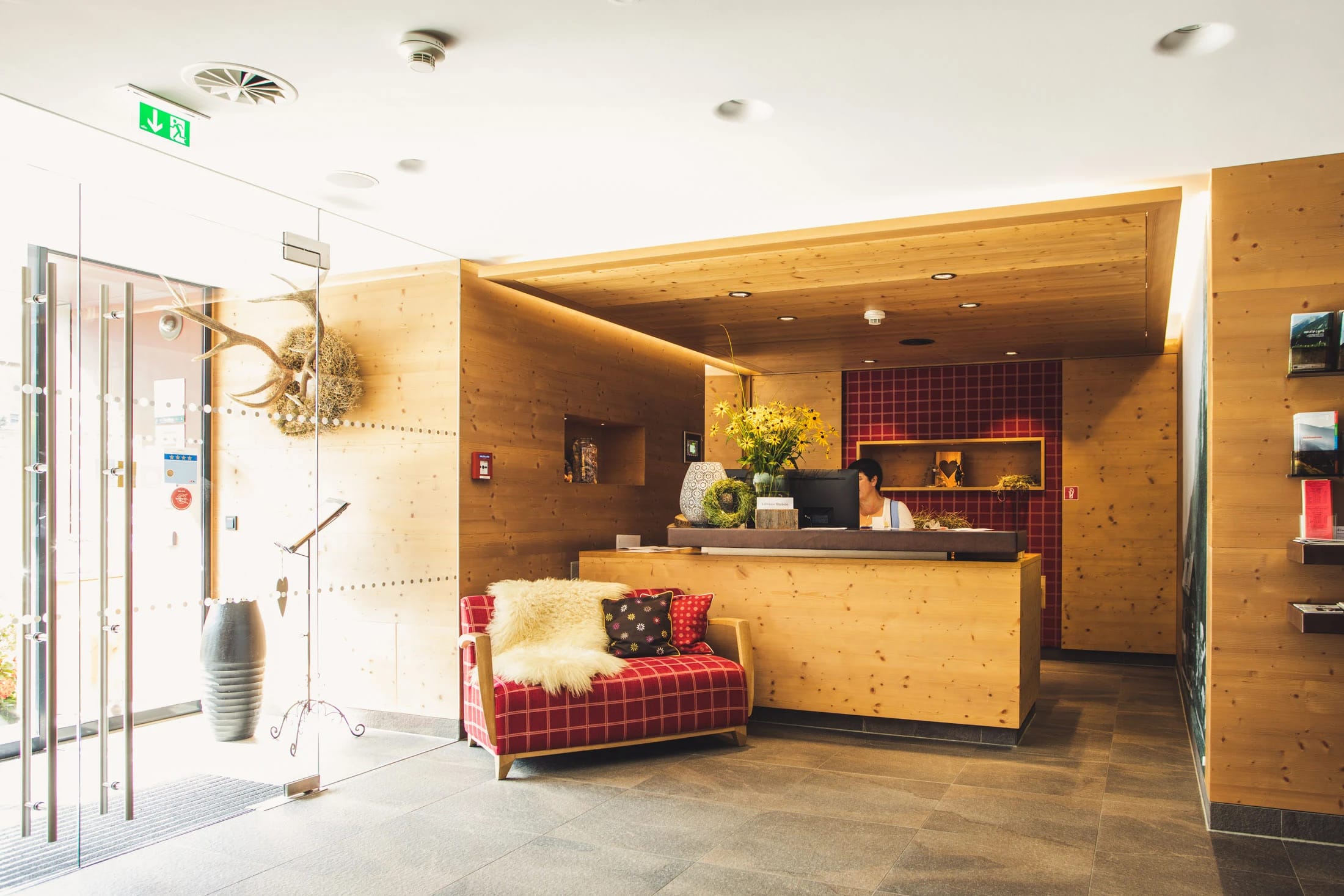Rezeption mit Holztheke, rot kariertem Sofa und Geweih an der Wand