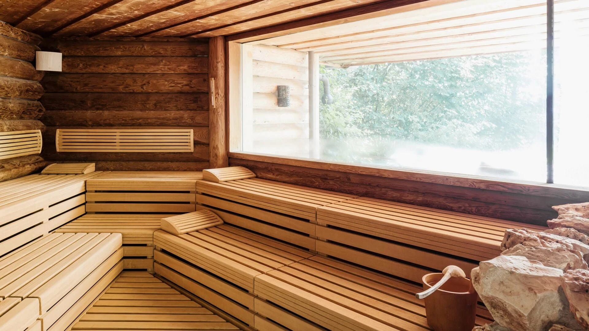 Sauna aus hellem Holz mit Stufenbänken und großem Fenster ins Grüne