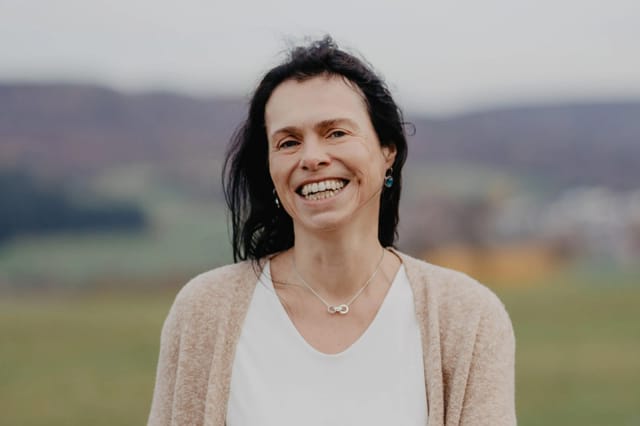 Porträt von Sabine Czilwa, lächelnd im Freien mit Hügellandschaft im Hintergrund