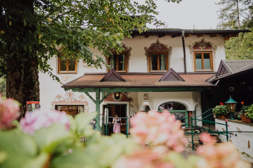 Außenansicht des traditionellen Alpenhauses mit bemalter Fassade, Giebeldach und Blumen im Vordergrund