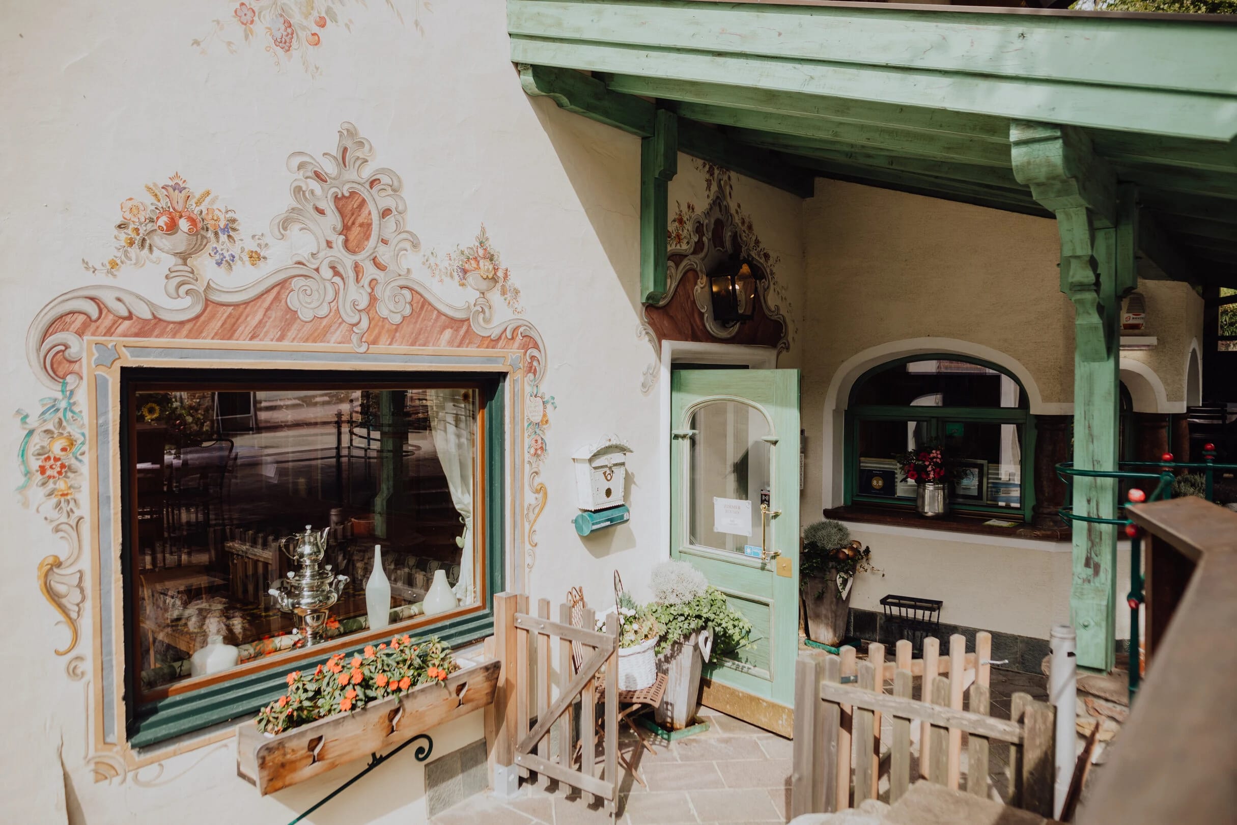Bemalte Hausfassade mit geschnitzten Holzbalken und Blumenschmuck im Eingangsbereich