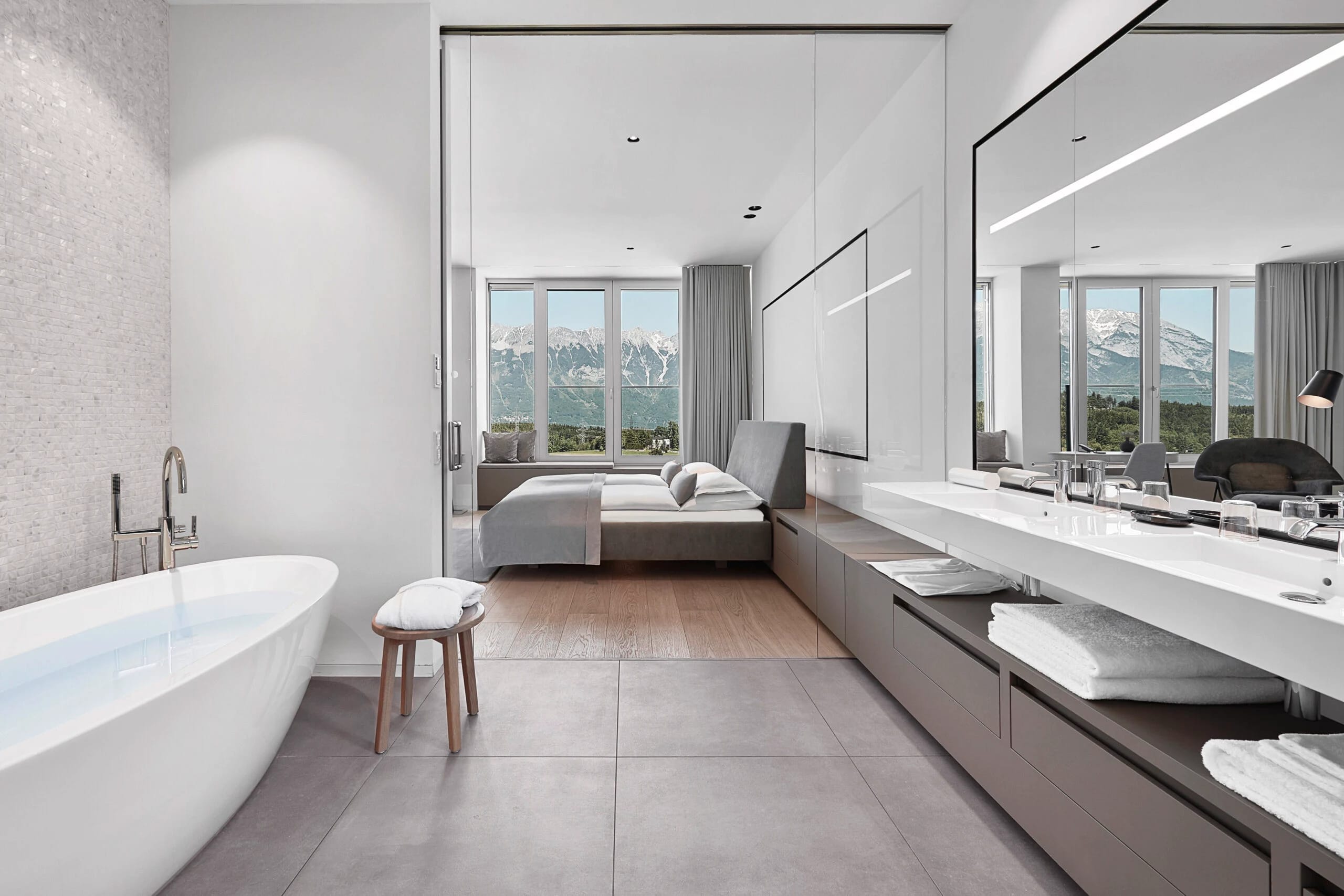 Badezimmer mit freistehender Wanne und langem Doppelwaschtisch, offener Blick ins Schlafzimmer und auf die Berge