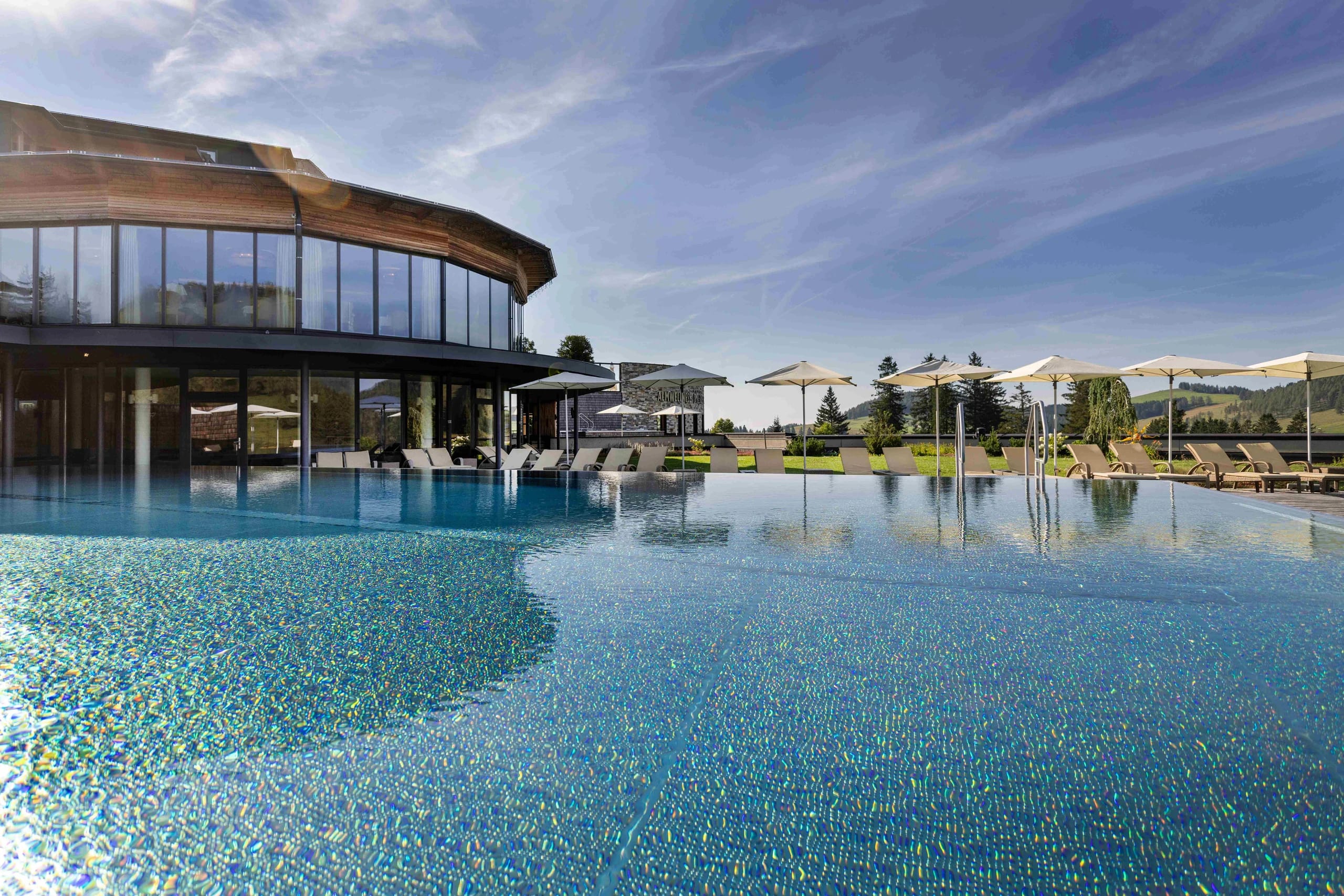 Außenpool mit Sonnenschirmen und Liegen neben dem runden verglasten Spa-Gebäude