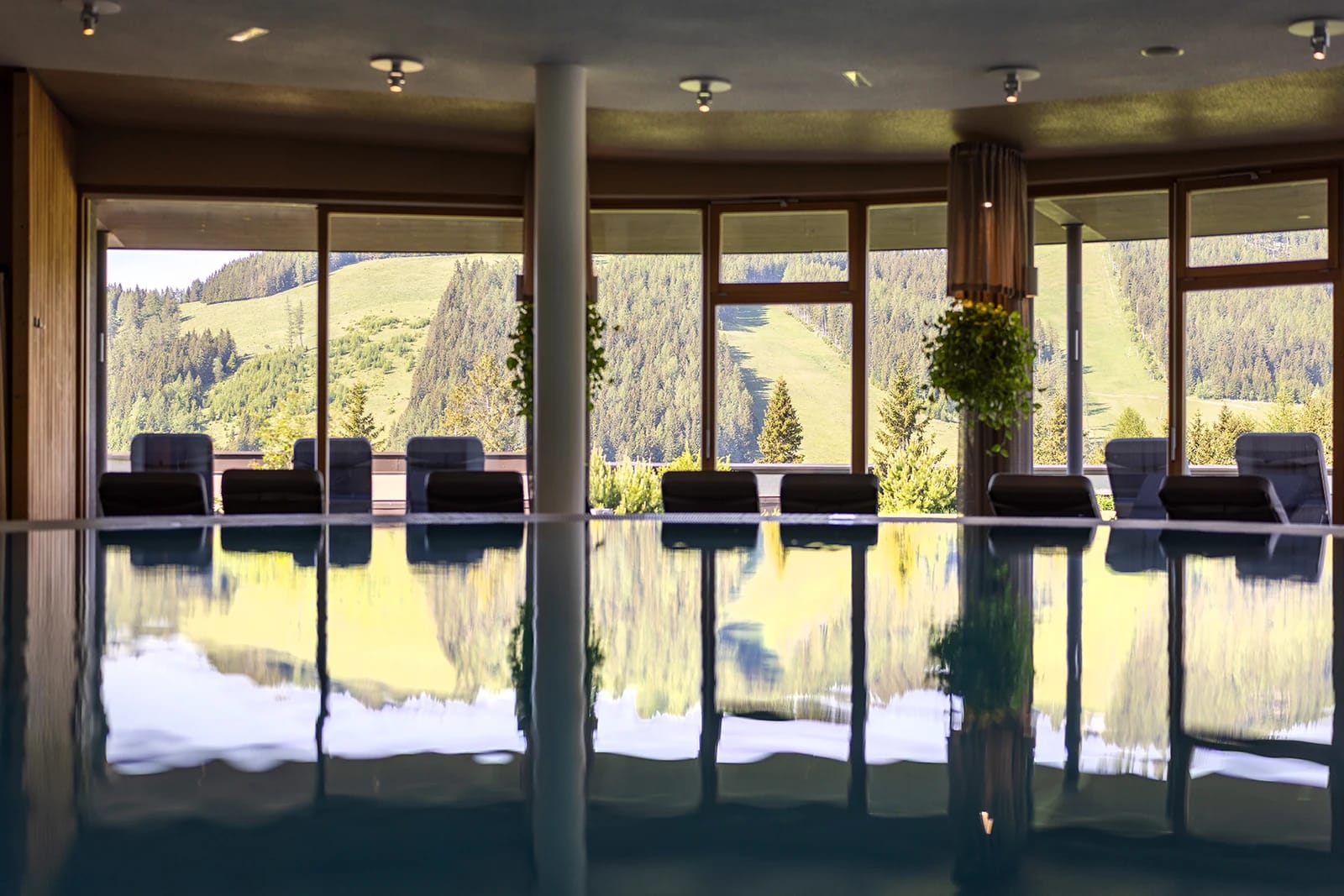 Innenpool mit Panoramafenstern, Liegestühlen und Blick auf Wald und Wiesen
