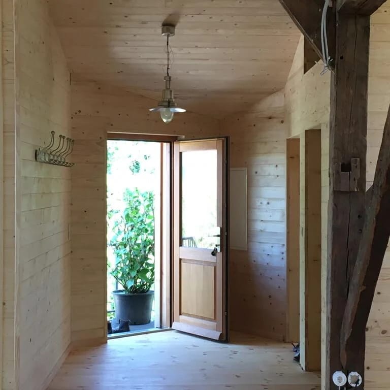 Eingangsdiele mit Holzverkleidung, Garderobenhaken und offener Tür zum Garten