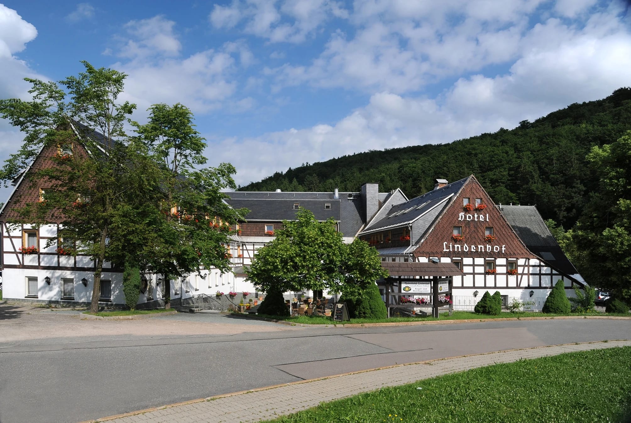 Langgestrecktes Fachwerkhaus des Hotels vor bewaldetem Hang unter blauem Himmel