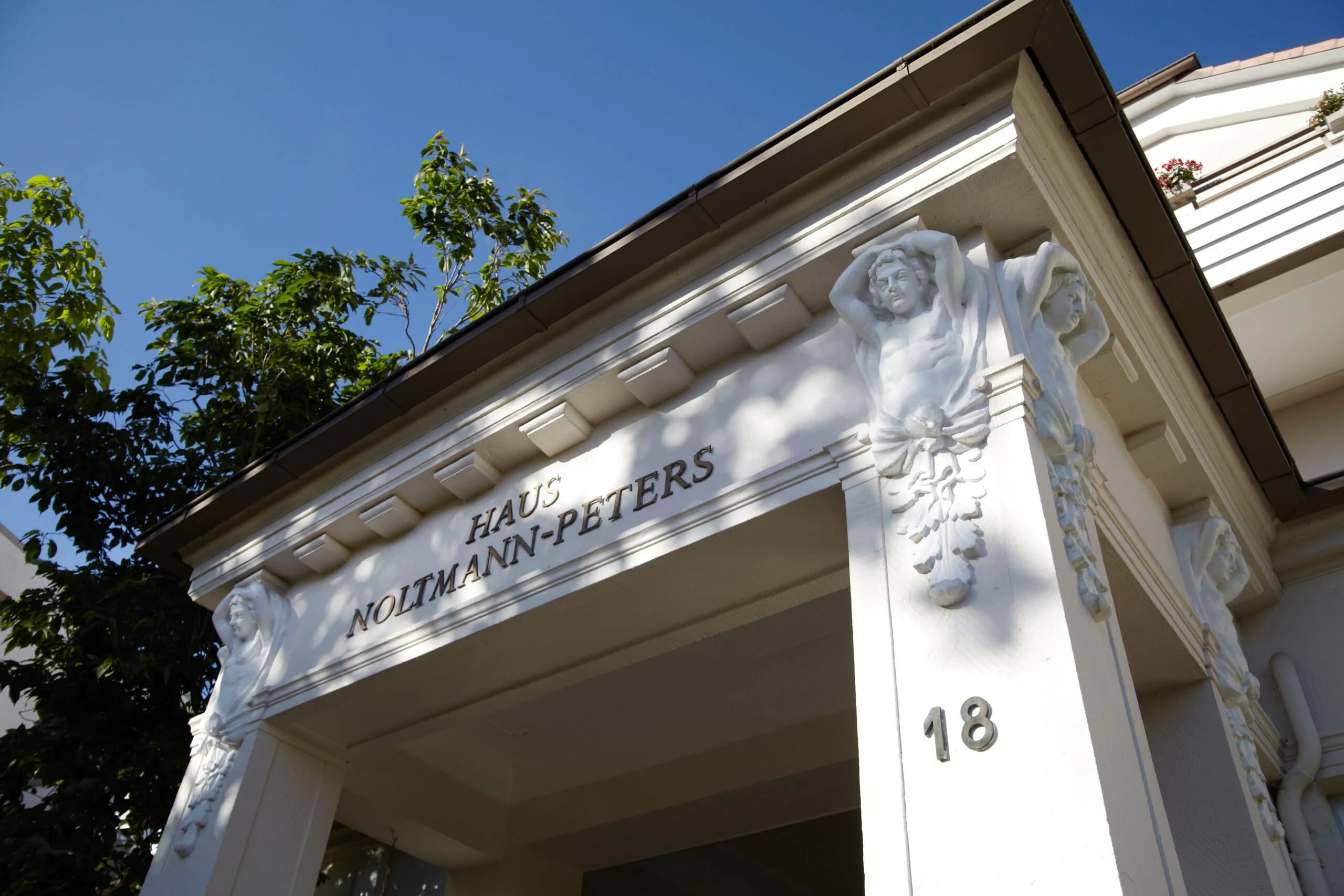 Säulenportal des Hauses mit dem Schriftzug Haus Noltmann-Peters und Stuckfigur vor blauem Himmel