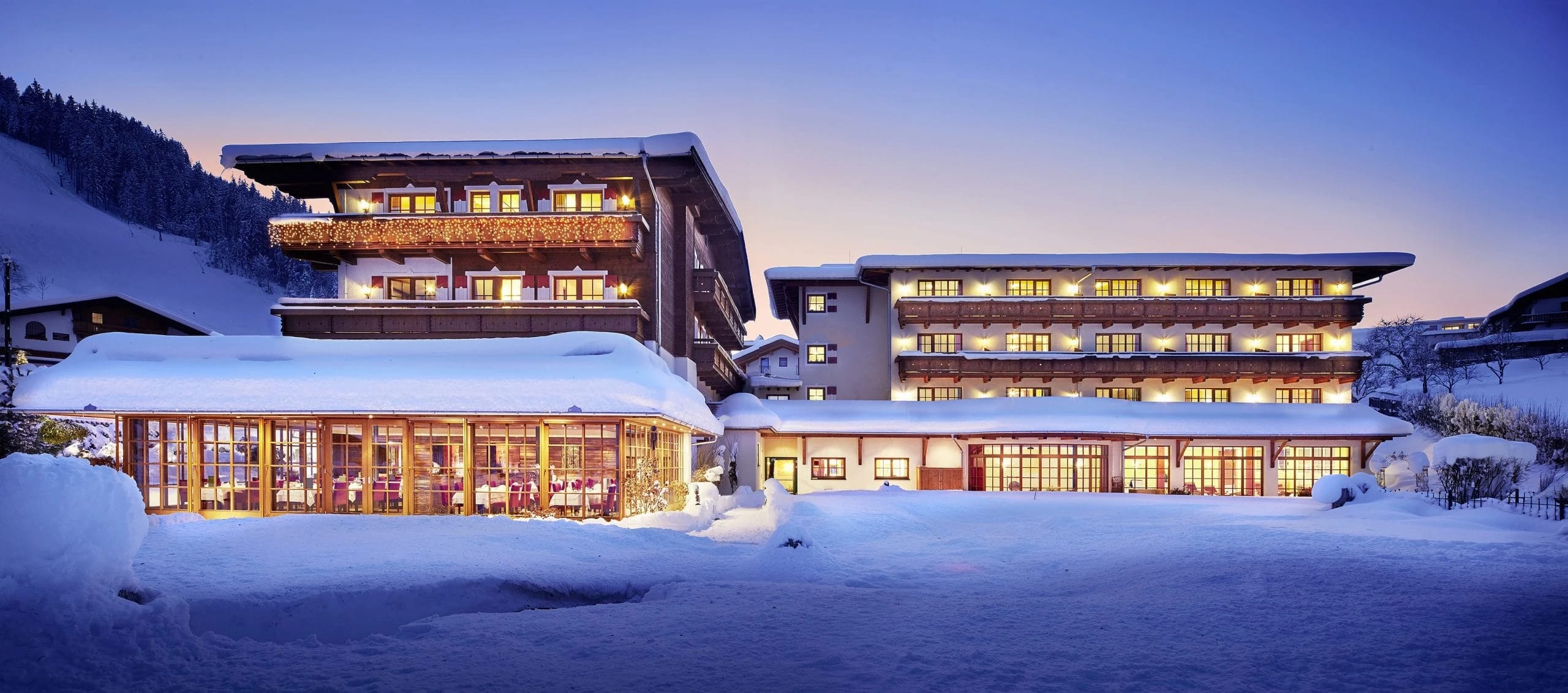 Verschneites Haus mit beleuchteten Fenstern und verglastem Wintergarten in der Abenddämmerung