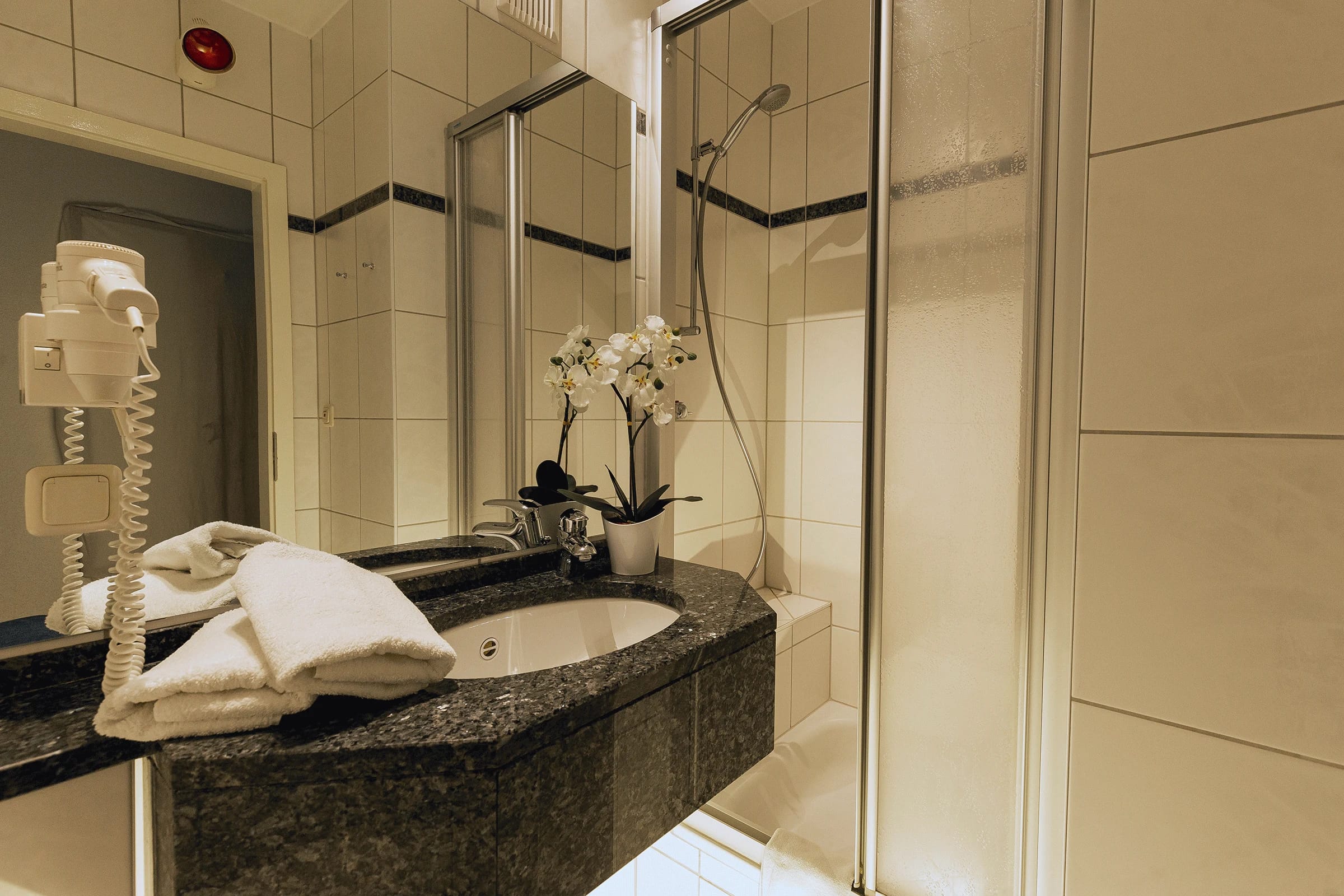 Badezimmer mit Granitwaschtisch, Spiegel, Dusche und Orchidee