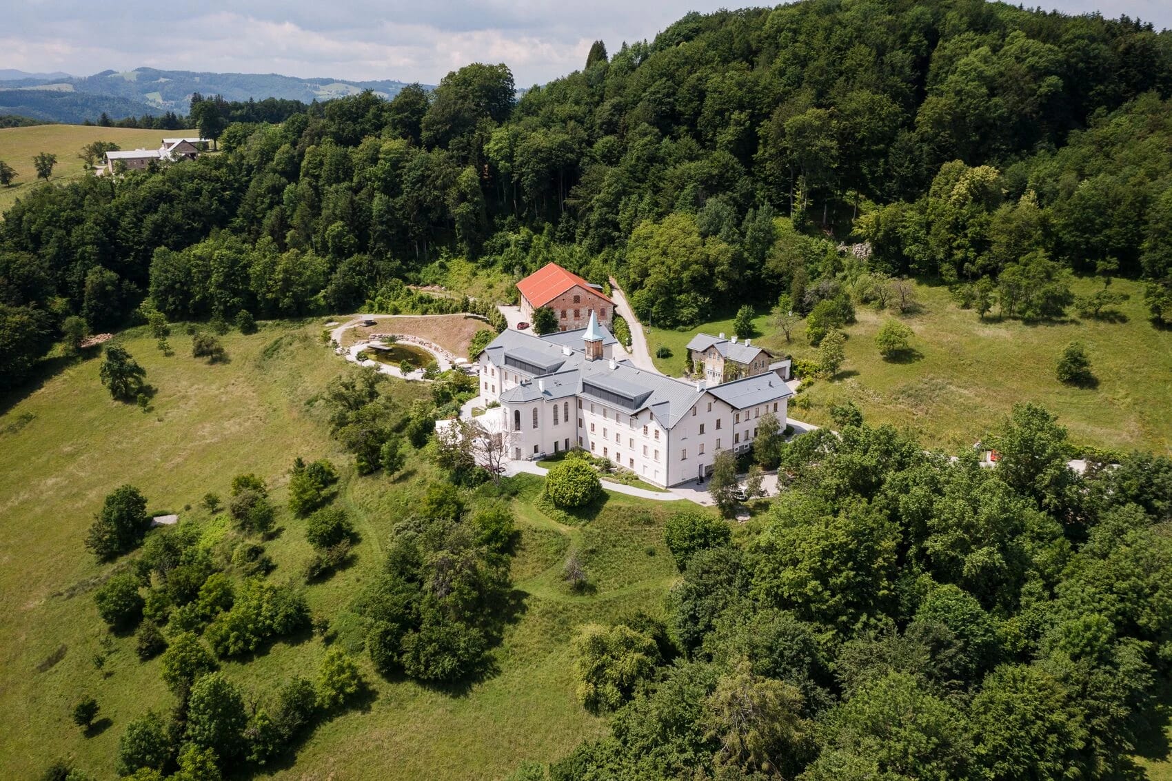 Luftaufnahme der weißen Klosteranlage mit rotem Turmdach zwischen Wiesen und Wald
