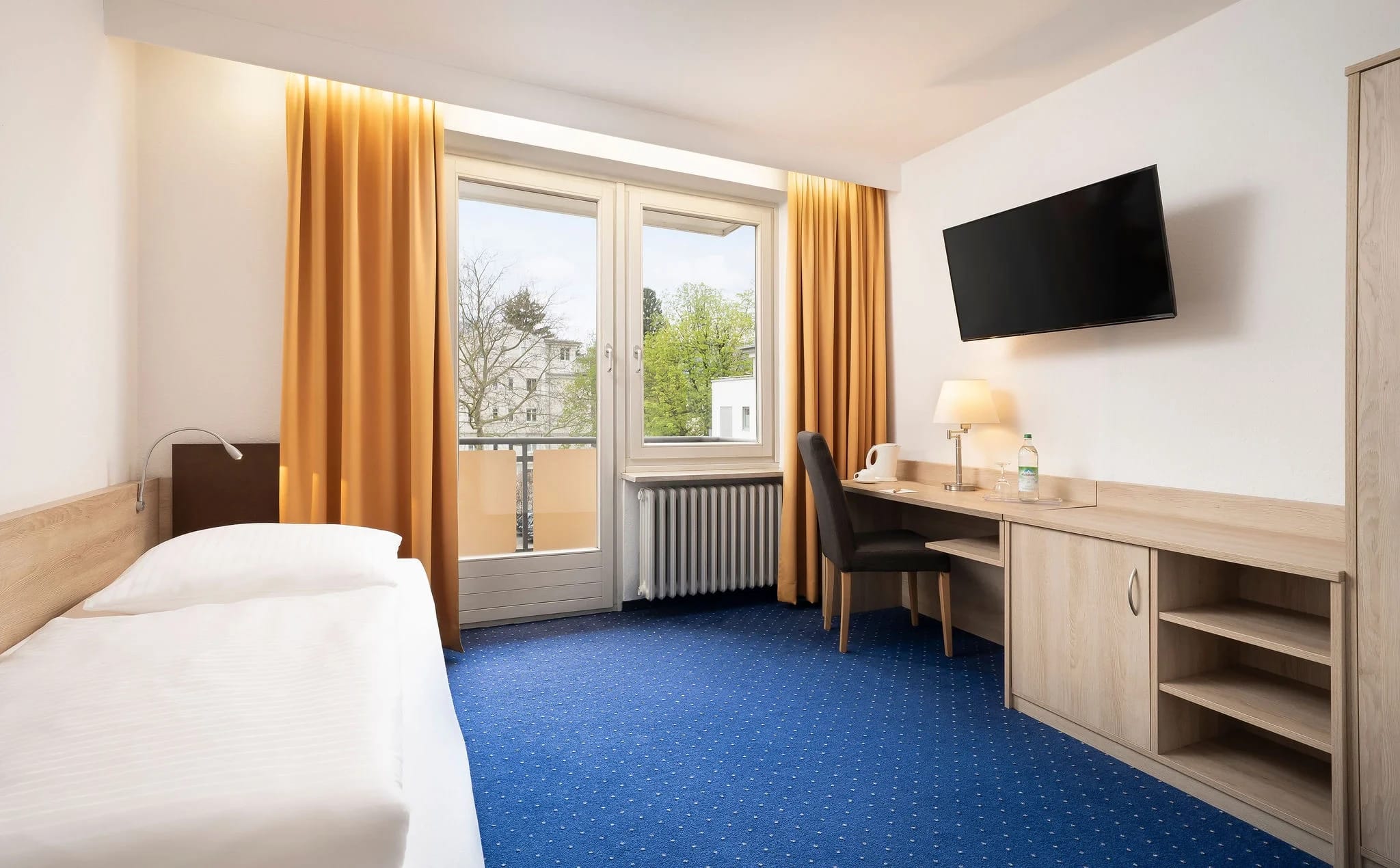 Zimmer mit Bett, Schreibtisch und Balkontür