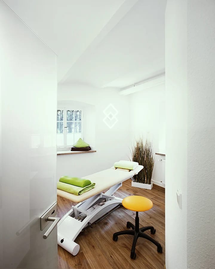 Behandlungsraum mit Liege, grünen Handtüchern, Rollhocker und kleinem Fenster