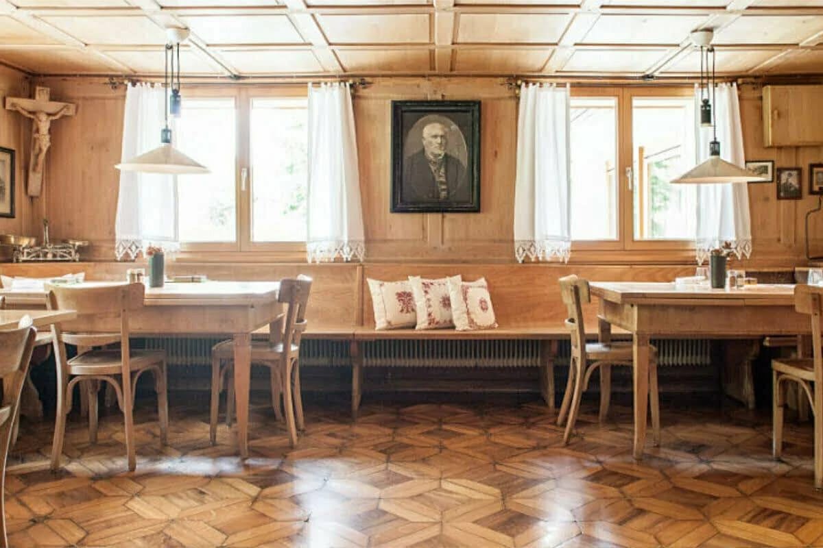 Traditionelle Stube mit Holztäfelung, langer Sitzbank, Holztischen und Parkettboden