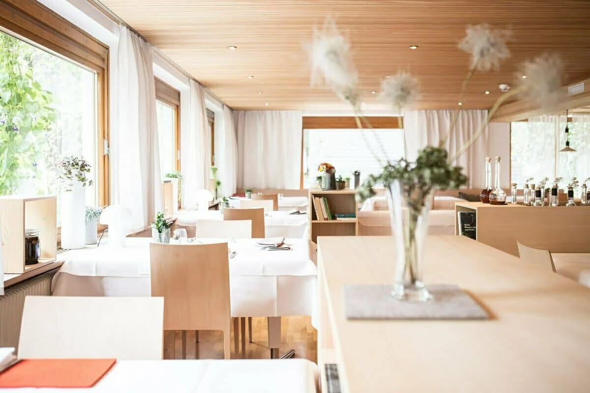 Heller Restaurantraum mit weiß eingedeckten Tischen, Holzdecke und großen Fenstern