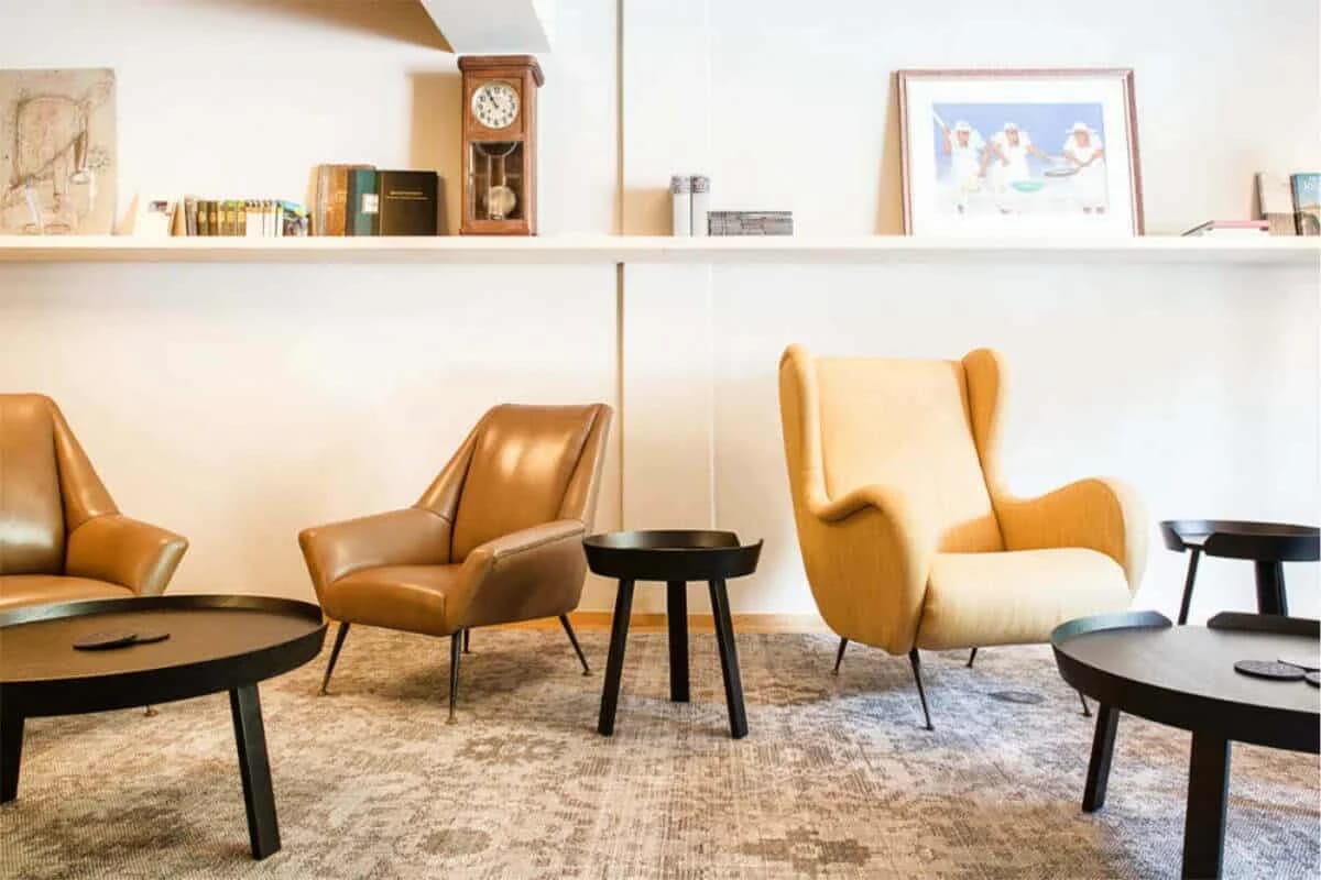 Lounge mit Ledersesseln, runden Beistelltischen, Bücherregal und gemustertem Teppich