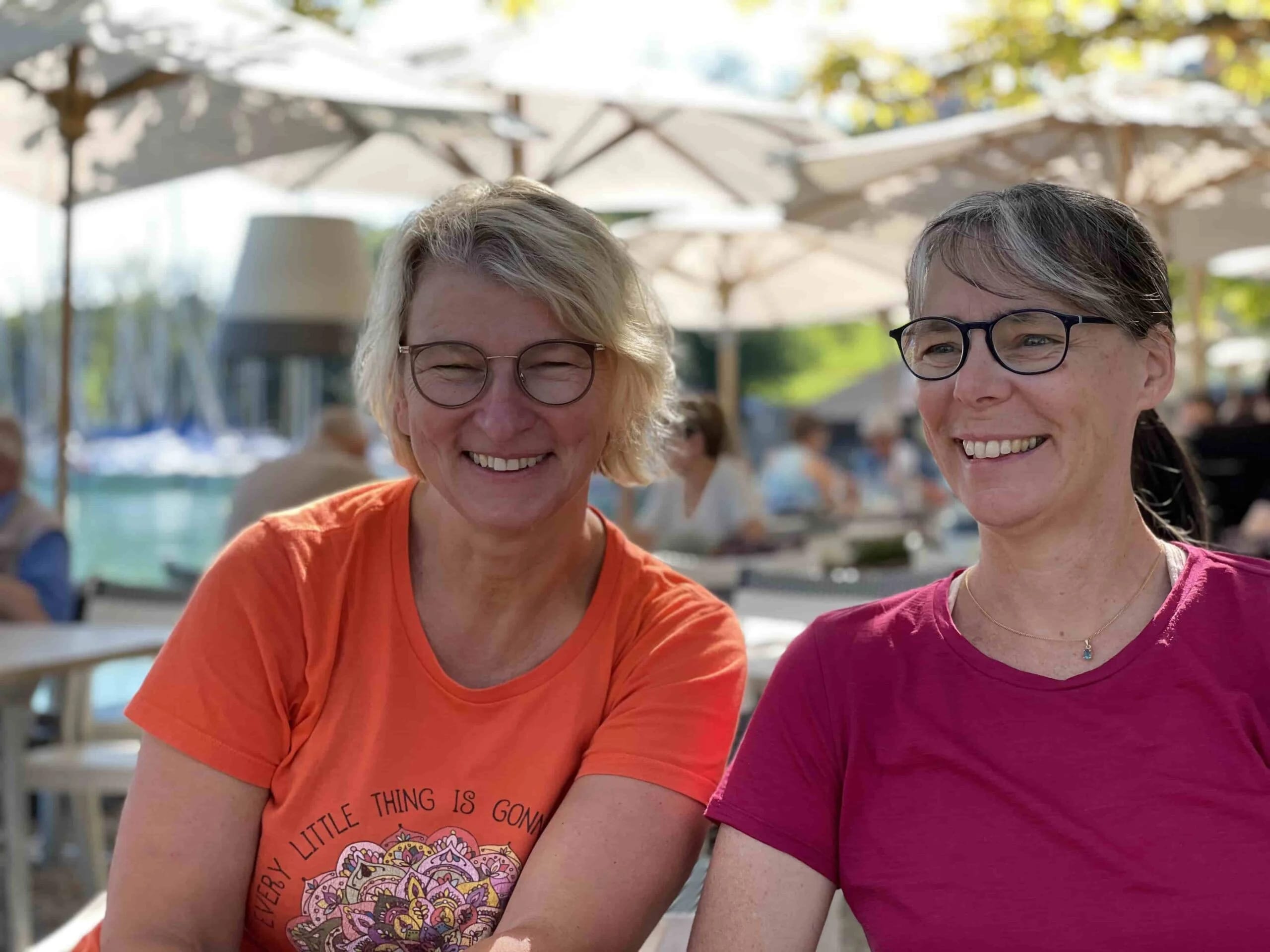 Sabine Wiemann und eine Begleiterin lachen gemeinsam an einem Seeufer-Café