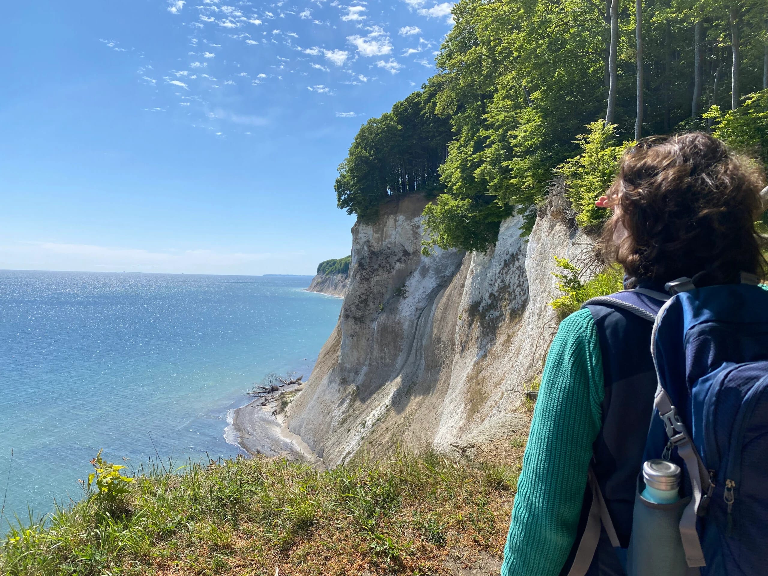 Wanderin mit Rucksack blickt vom Pfad auf die Kreidefelsen von Rügen