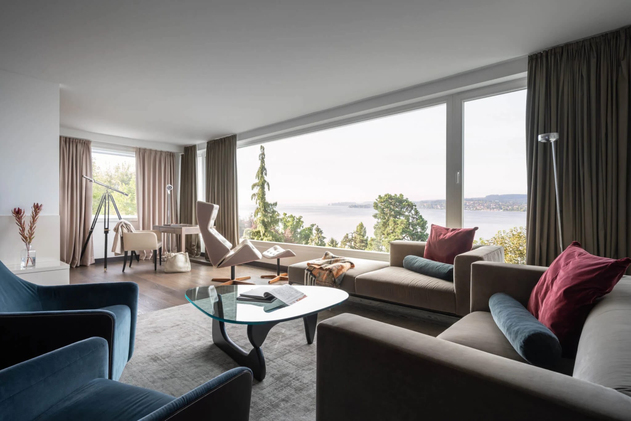 Wohnbereich einer Suite mit Sofas, Sesseln und Panoramafenster mit Seeblick