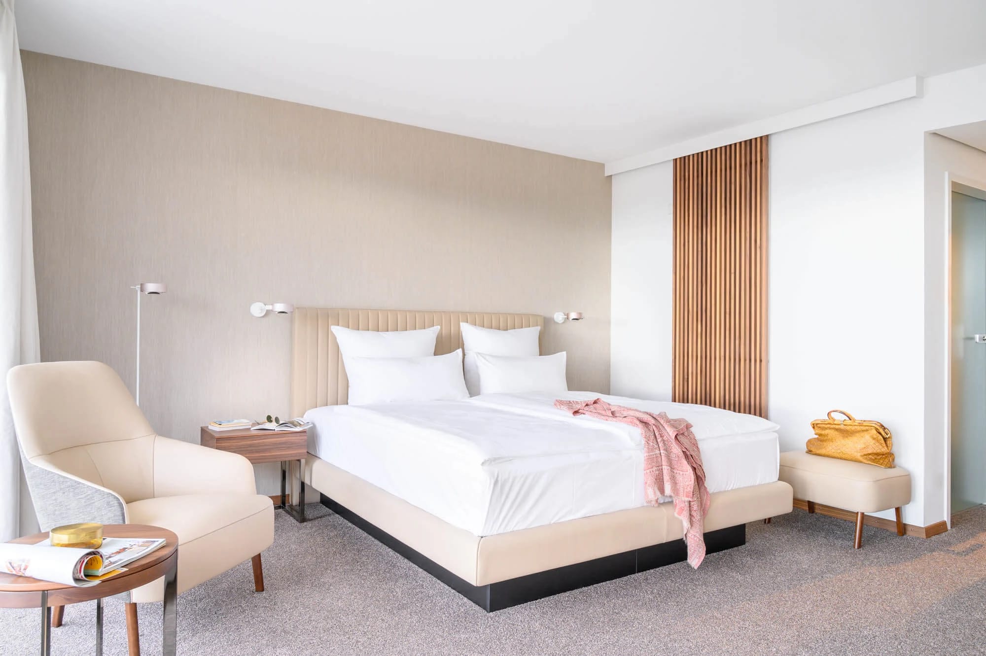 Modernes Schlafzimmer mit Doppelbett, hellem Sessel und Holzlamellen an der Wand