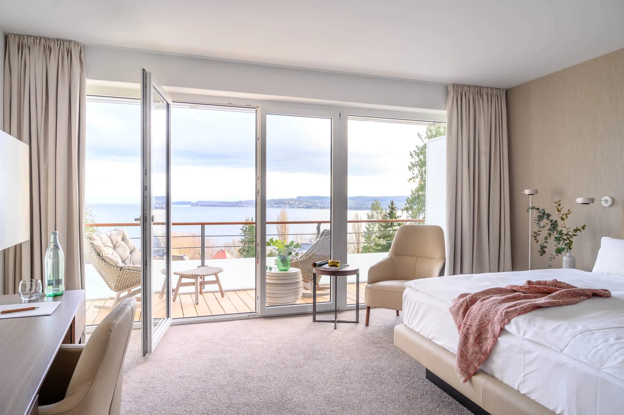 Helles Zimmer mit Doppelbett, Schreibtisch und offener Balkontür mit Blick auf den Bodensee