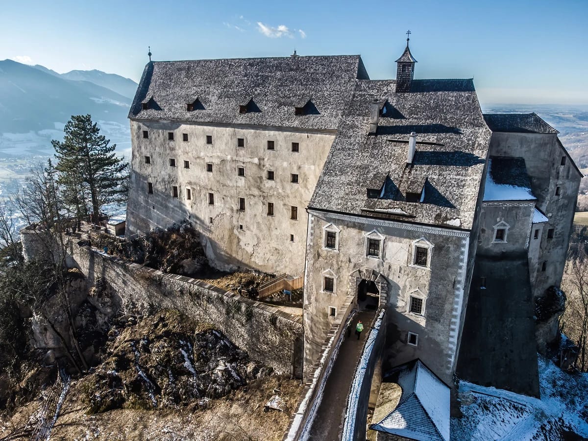 Luftaufnahme der Burg Altpernstein im Winter mit verschneiten Bergen im Hintergrund
