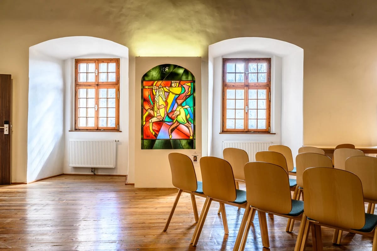 Heller Seminarraum mit Rundbogenfenstern, Buntglasbild und Stuhlreihe