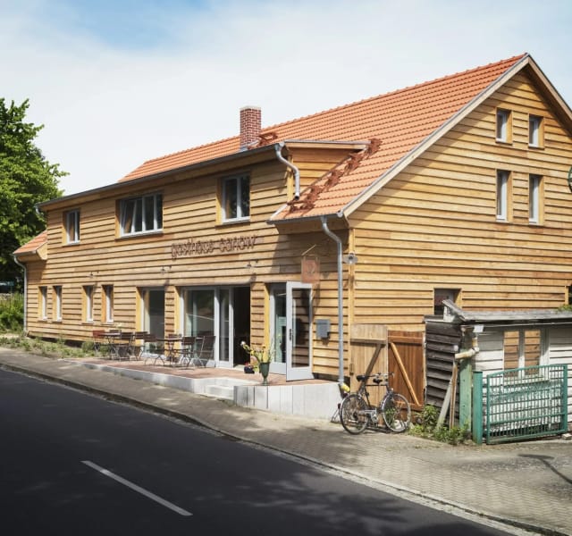 Außenansicht des Gasthauses mit Holzfassade, rotem Ziegeldach und Terrasse an der Straße