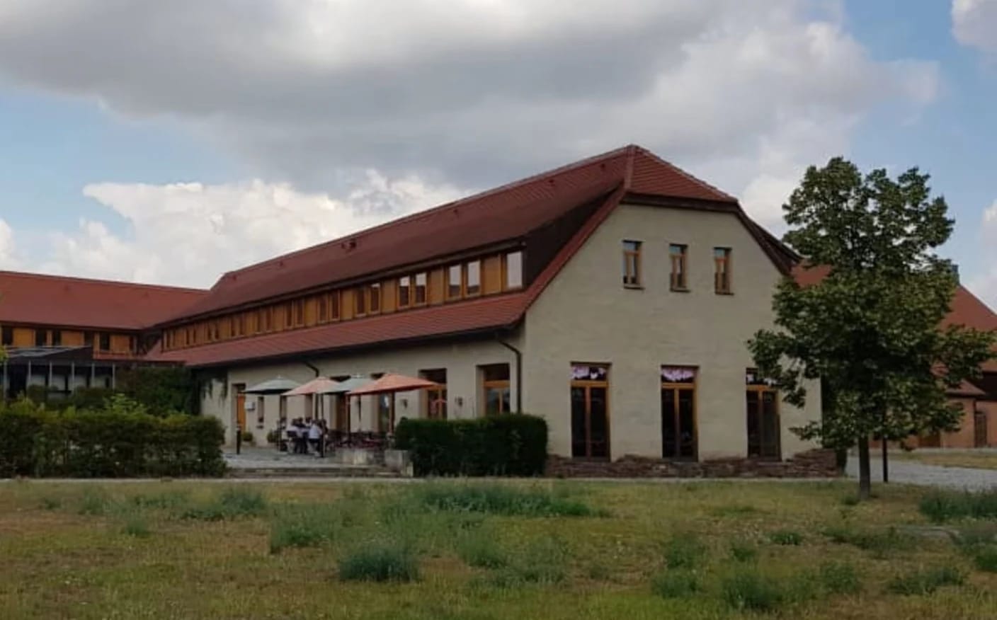 Langgestrecktes Gebäude mit rotem Ziegeldach und Freisitz mit Sonnenschirmen davor
