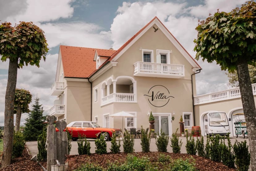 Cremefarbene Villa mit rotem Ziegeldach, Balkonen und Oldtimer vor dem Haus