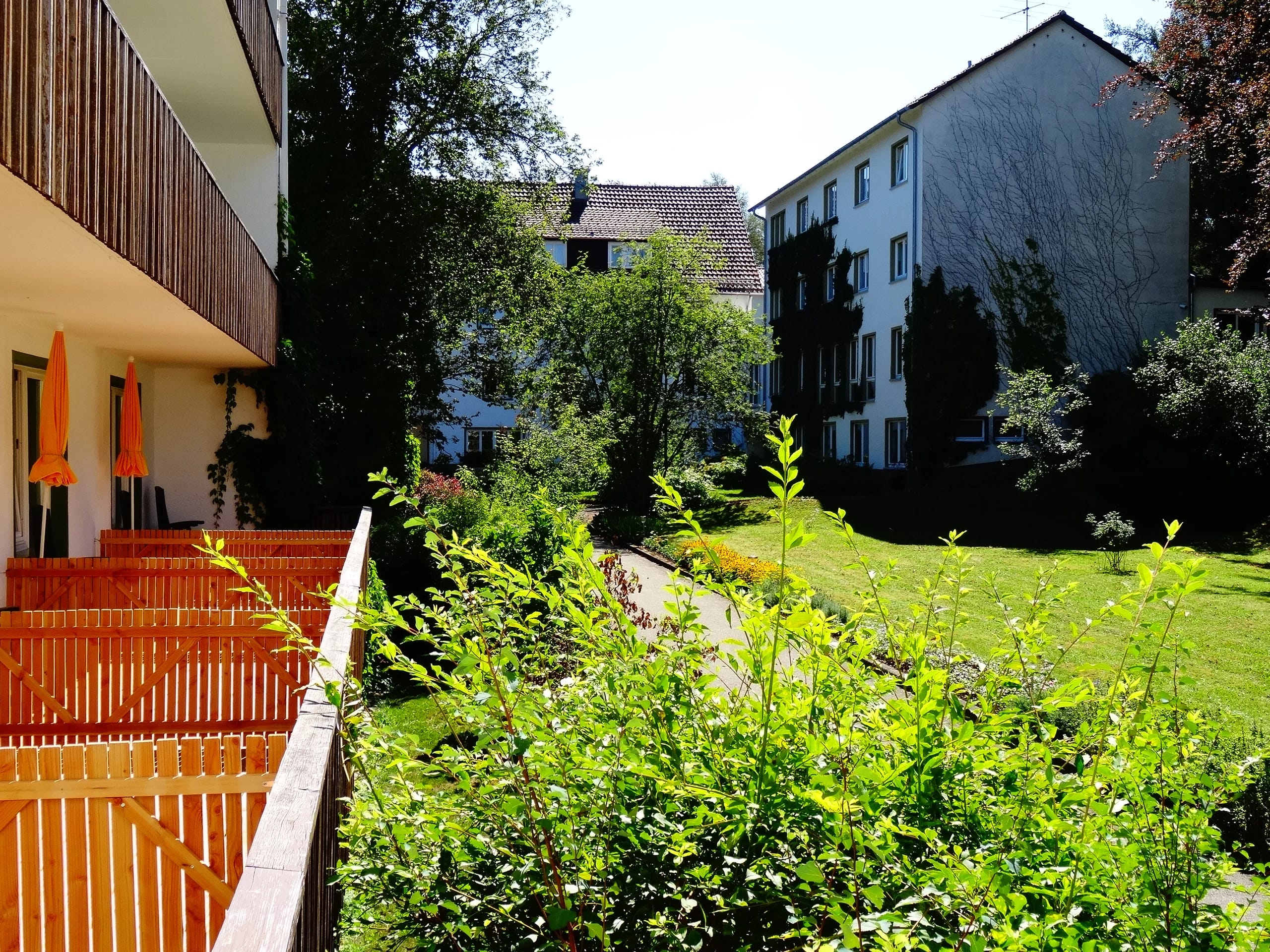Blick vom Balkon über den grünen Garten auf die Gebäude des Hauses