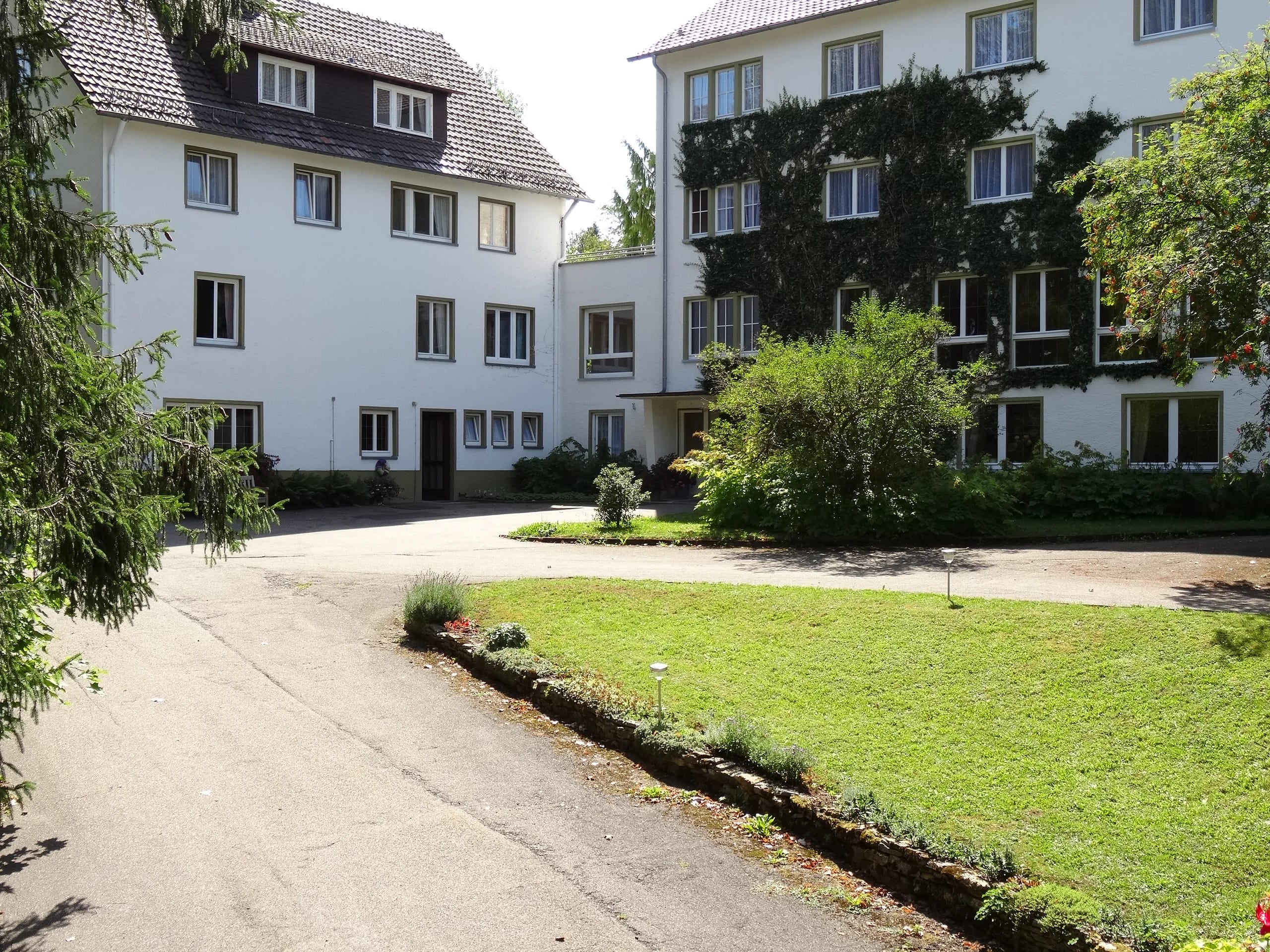 Weiße Gebäude des Hauses mit Zufahrt, Rasenfläche und hohen Bäumen