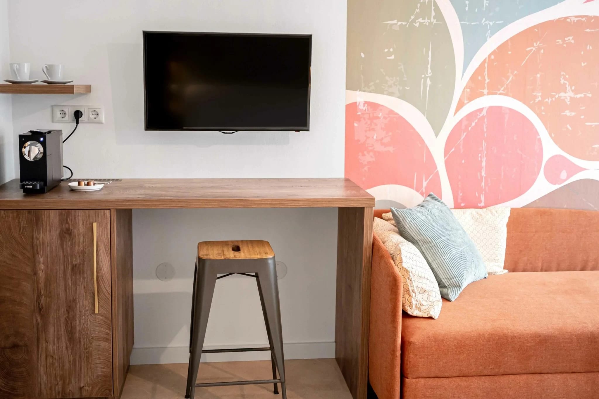Zimmer mit orangefarbenem Sofa, Holzschreibtisch, Barhocker und Fernseher