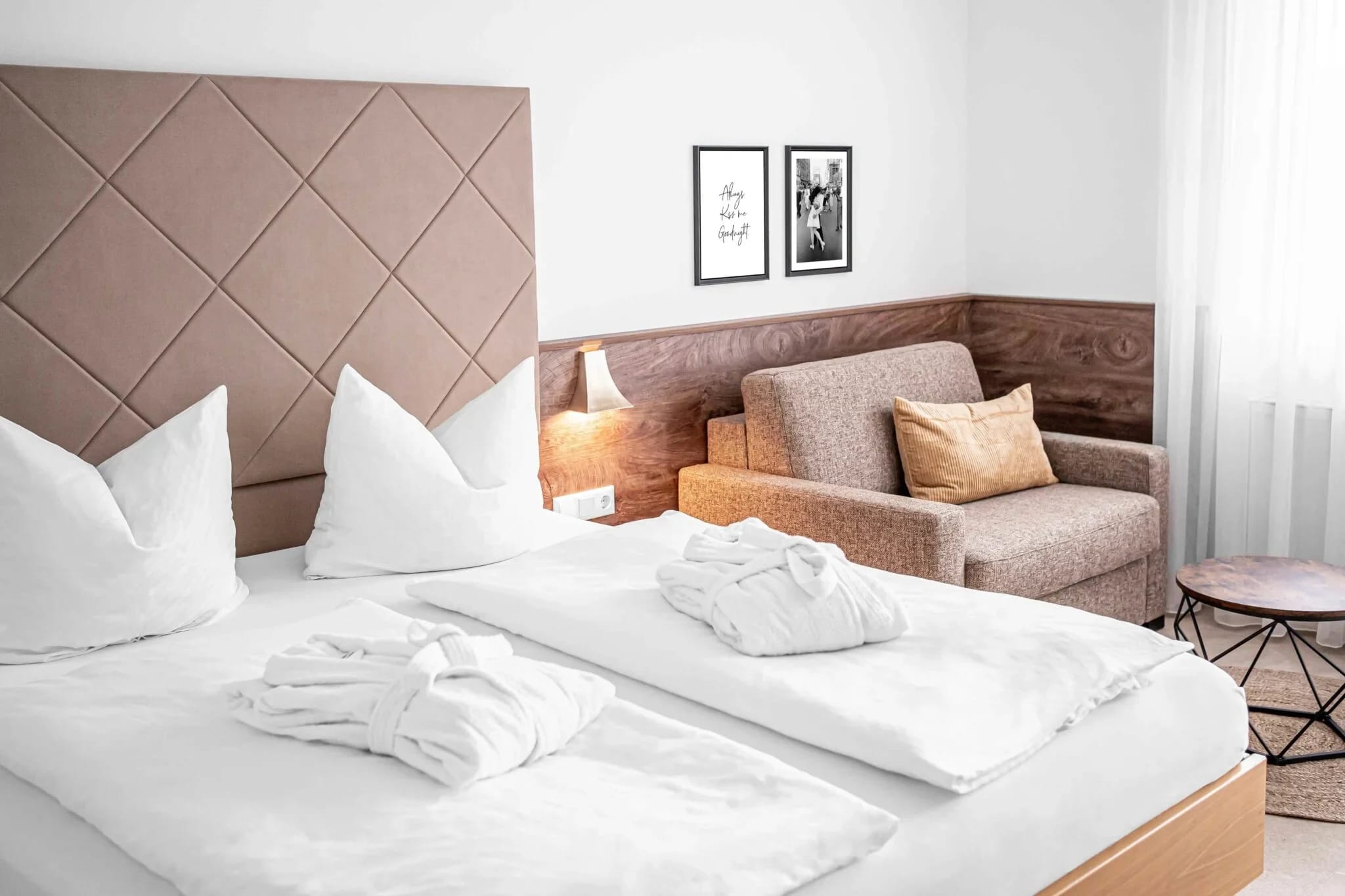 Helles Doppelzimmer mit weißer Bettwäsche, Bademänteln und Sofaecke